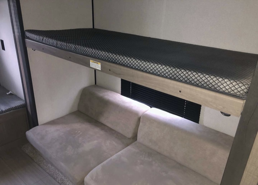 RV rental interior featuring a bunk bed over a plush sofa and window blinds, ideal for comfortable travel.. Keystone RV Hideout LHS 2021