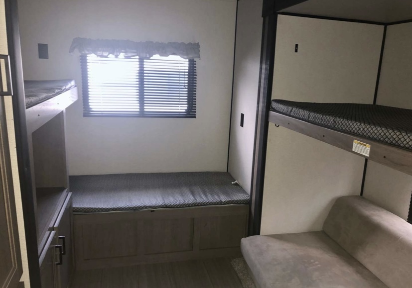RV rental bunkhouse: Bright interior with multiple bunks, a sofa, and a bench by a window, providing family sleeping space.. Keystone RV Hideout LHS 2021