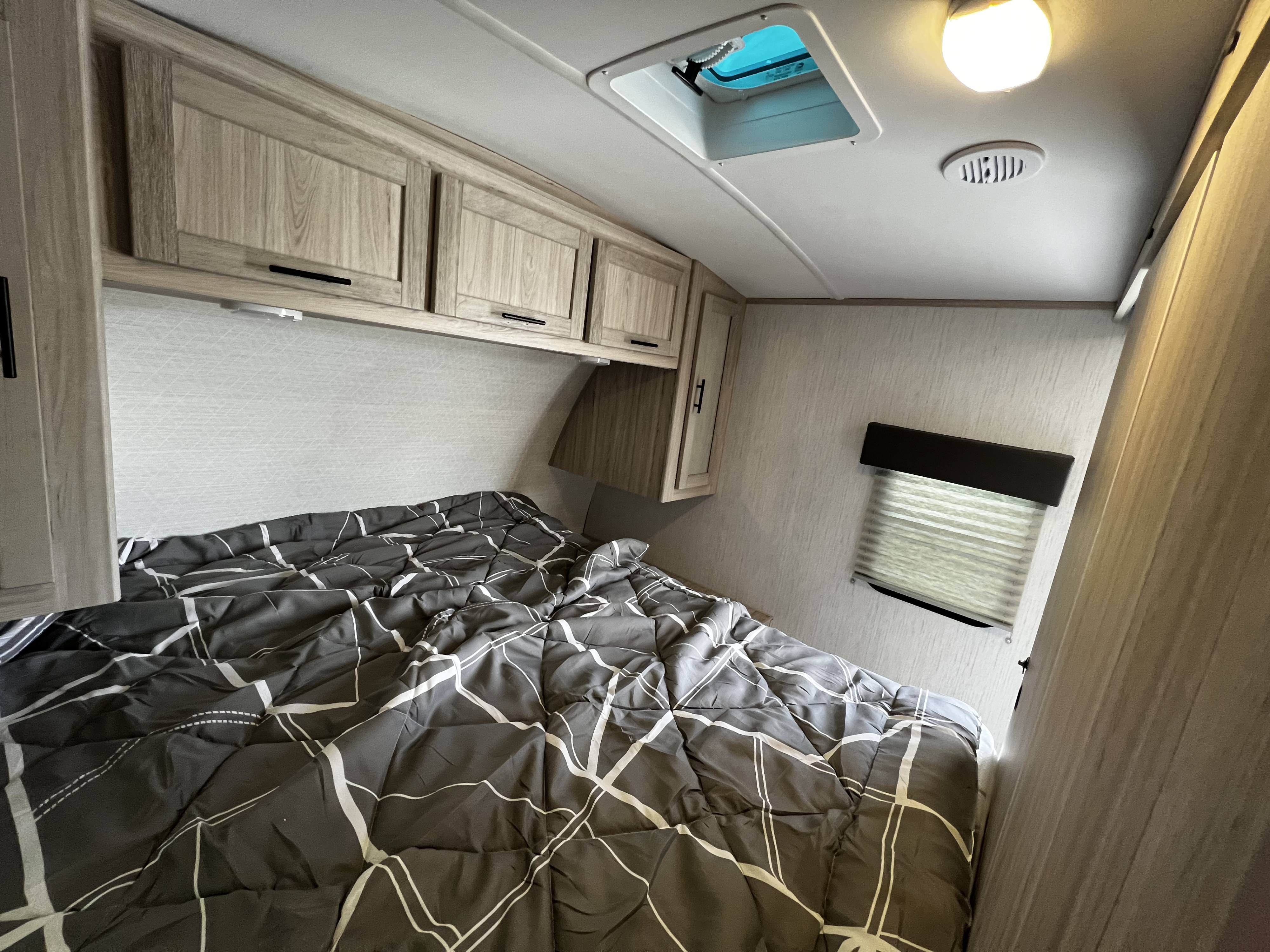 Cozy RV rental bedroom featuring a bed with a patterned comforter, overhead cabinets, a skylight, and a window.. Cruiser Shadow Cruiser 240 BHS 2022