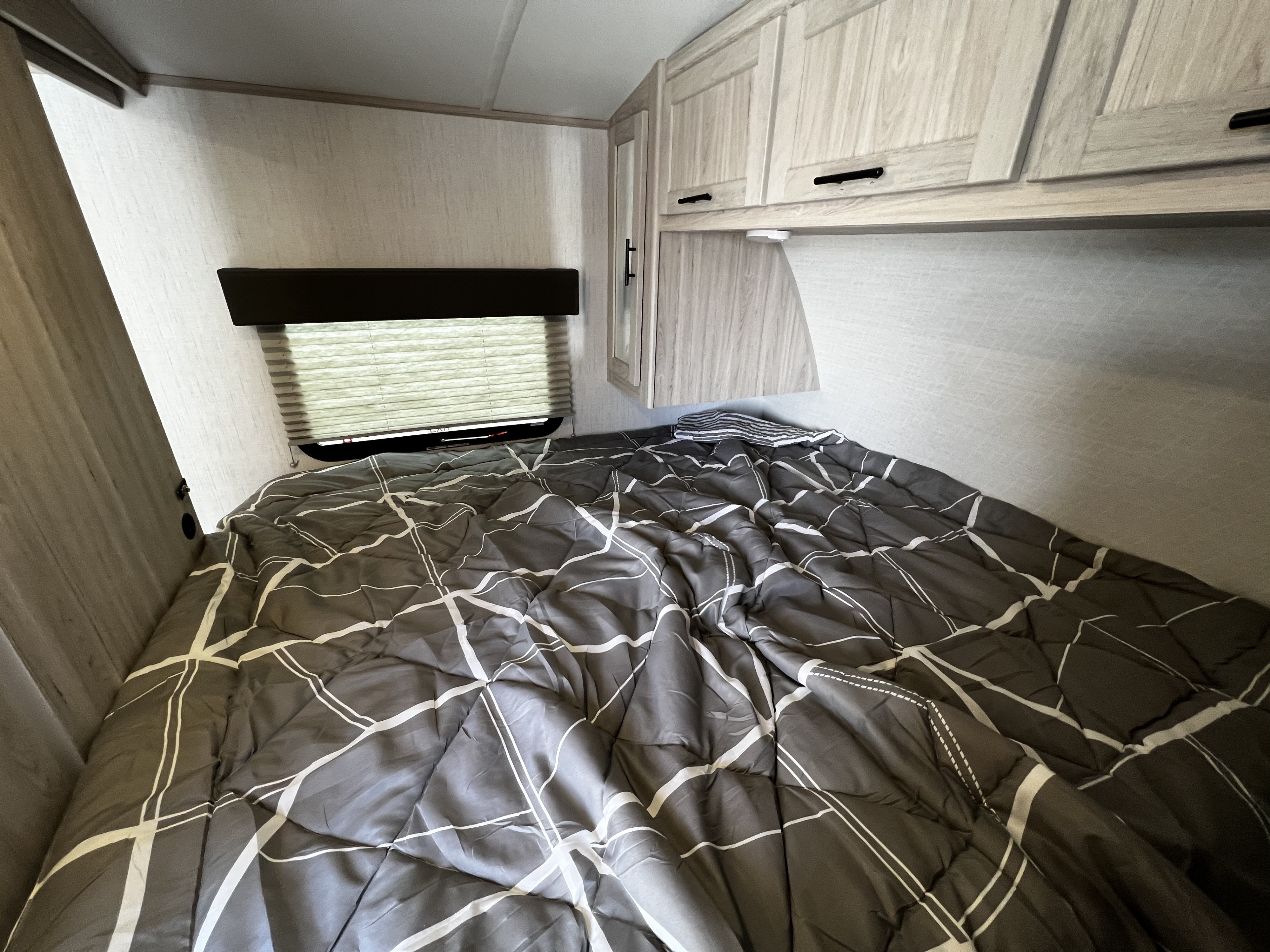 Cozy RV rental bedroom featuring a bed with modern gray comforter, window, and overhead storage.. Cruiser Shadow Cruiser 240 BHS 2022