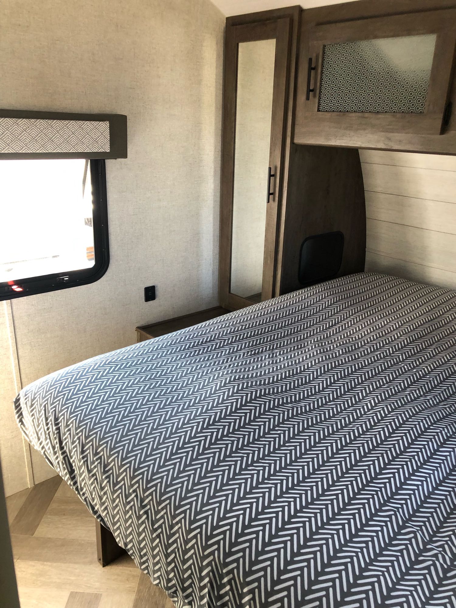 RV rental bedroom showing a patterned bed, mirrored cabinet, window, and modern finishes.. Forest River Wildwood 2020