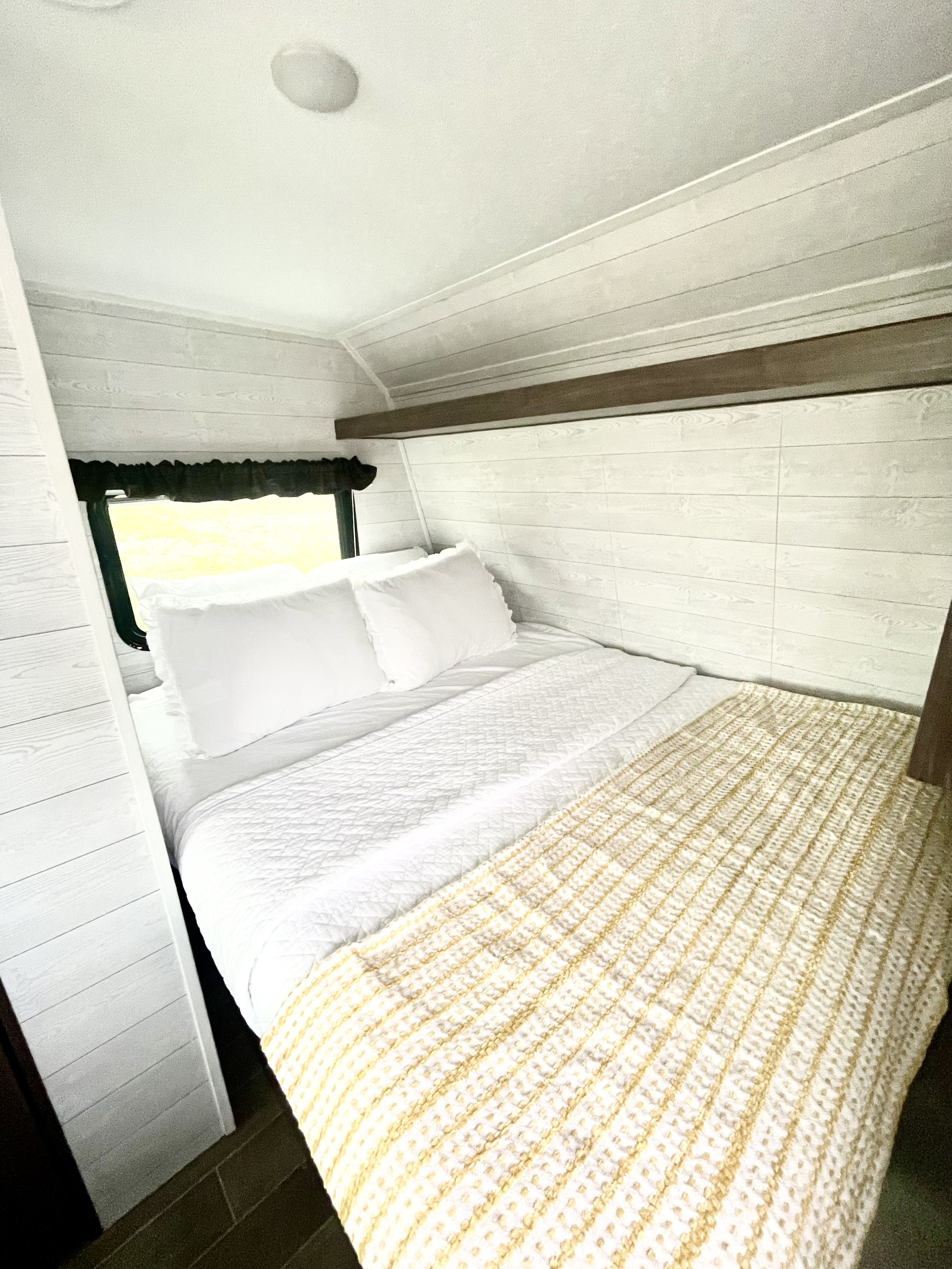 Cozy RV rental bedroom with a comfy bed, white bedding, a yellow throw, and stylish shiplap walls.. Keystone Hideout 2019