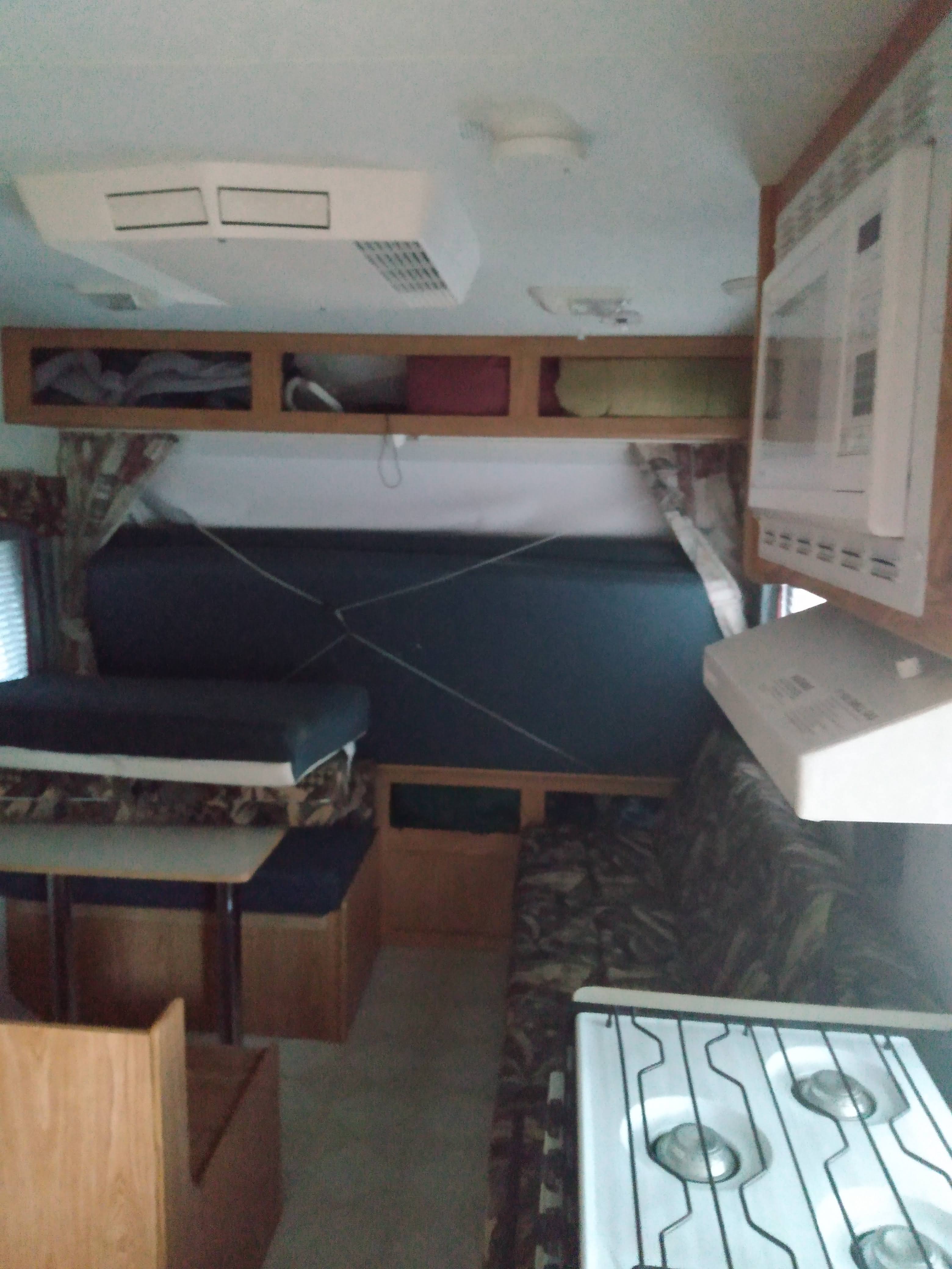 Cozy RV rental interior with dinette, bed, overhead storage, microwave, and stove for your travels.. Sportsmen Coyote 2002