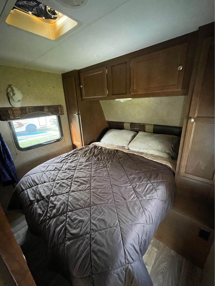 RV rental bedroom: a comfortable bed with a dark comforter, overhead cabinets, a window, and a ceiling vent in a camper.. Sport Trek Sport Trek Trailer 2015