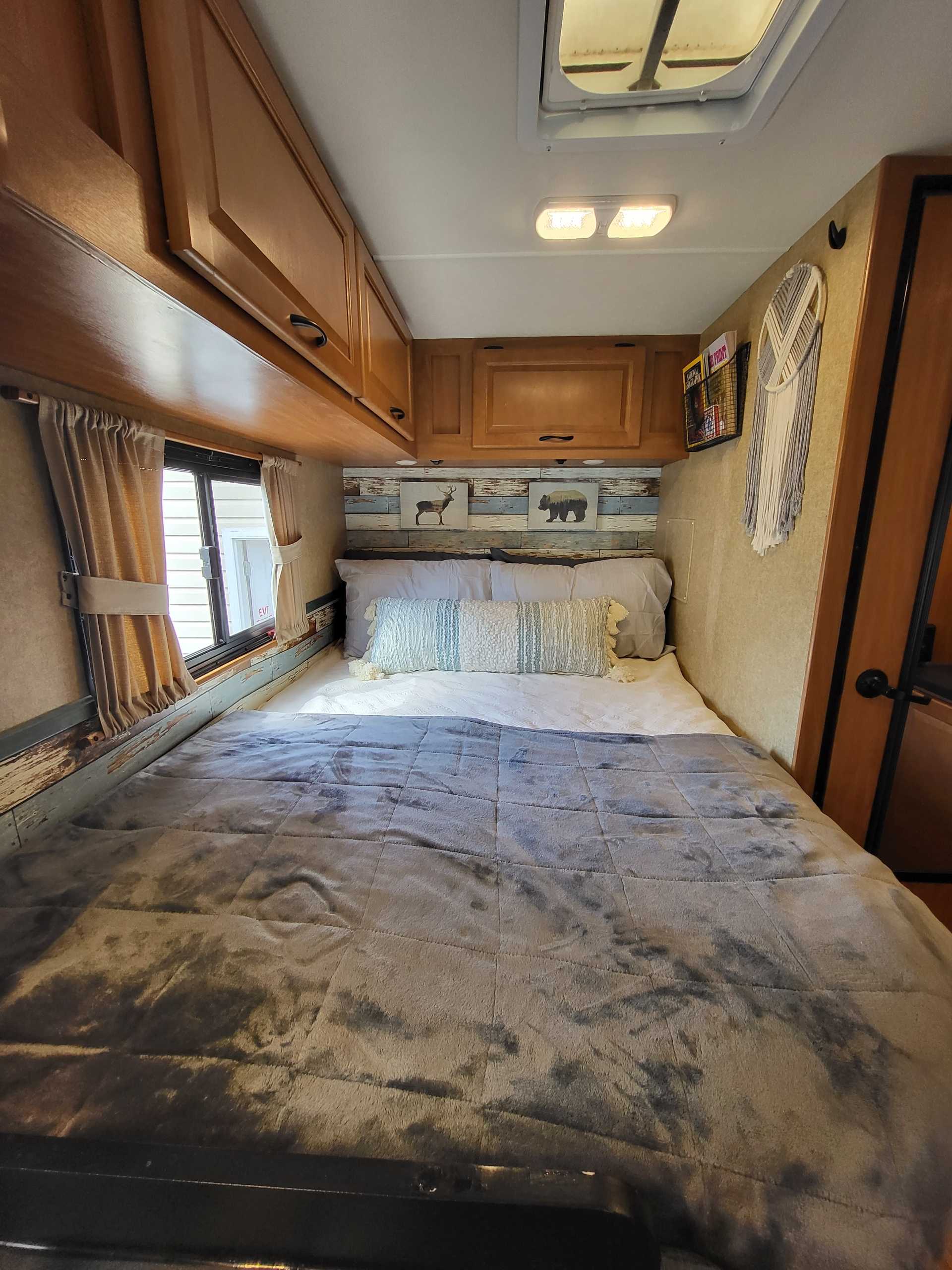 Cozy RV rental bedroom featuring a comfortable bed, overhead storage, and rustic decor with animal art.. Thor Majestic 2017