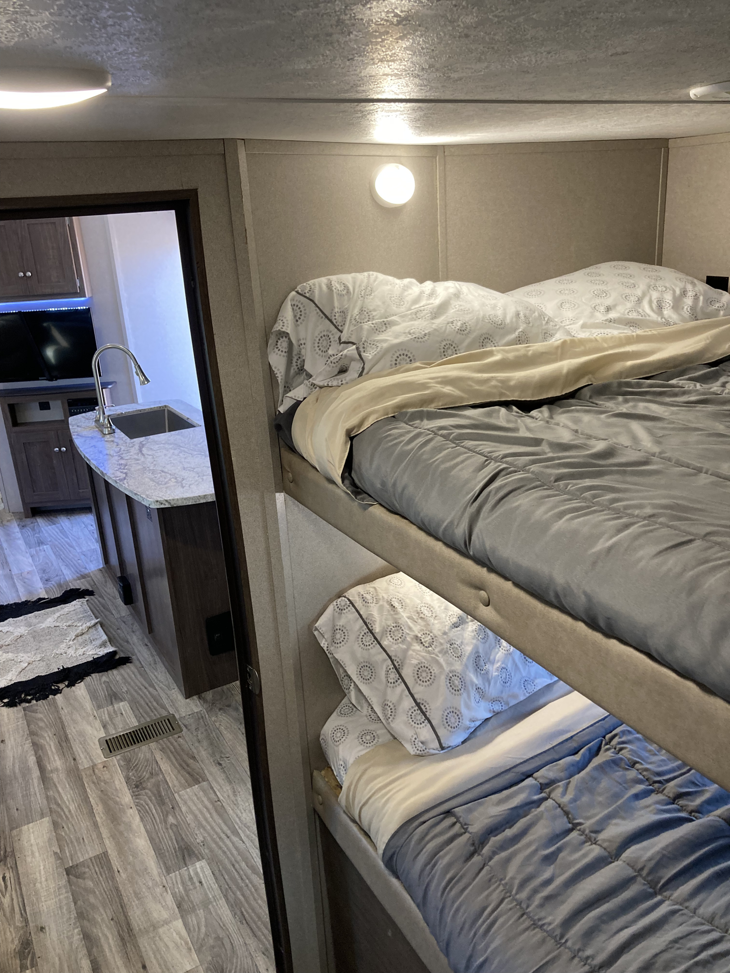 RV rental interior: view of bunk beds with bedding & a peek into the kitchen area with sink and TV beyond.. Keystone Hideout 2018