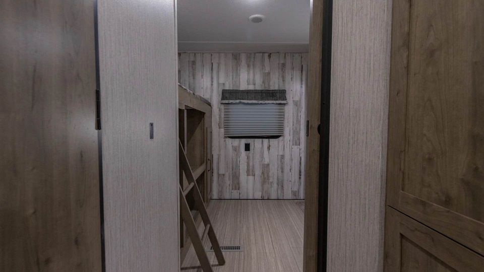 RV rental interior: bunk bed area with a ladder, rustic wood paneling, and window blinds, viewed from a hallway.. Forest River Palomino Puma XLE Lite 2021