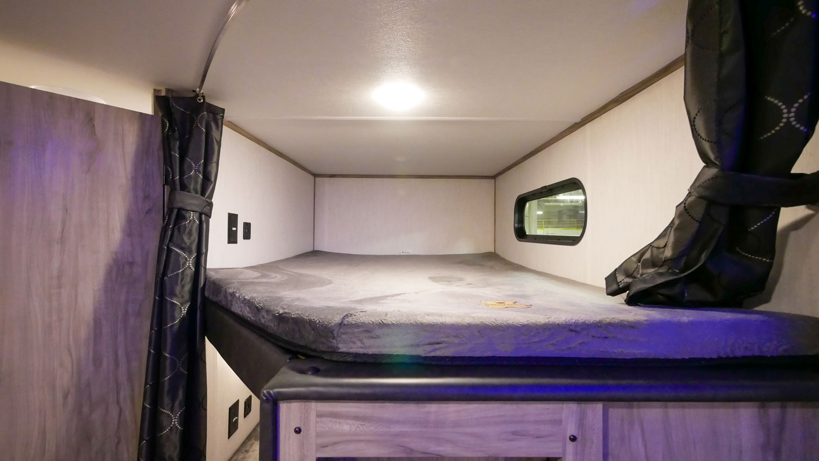 This RV rental offers a cozy bunk bed area with a grey mattress, privacy curtains, and a small window for natural light.. Forest River Cherokee Alpha Wolf 2021