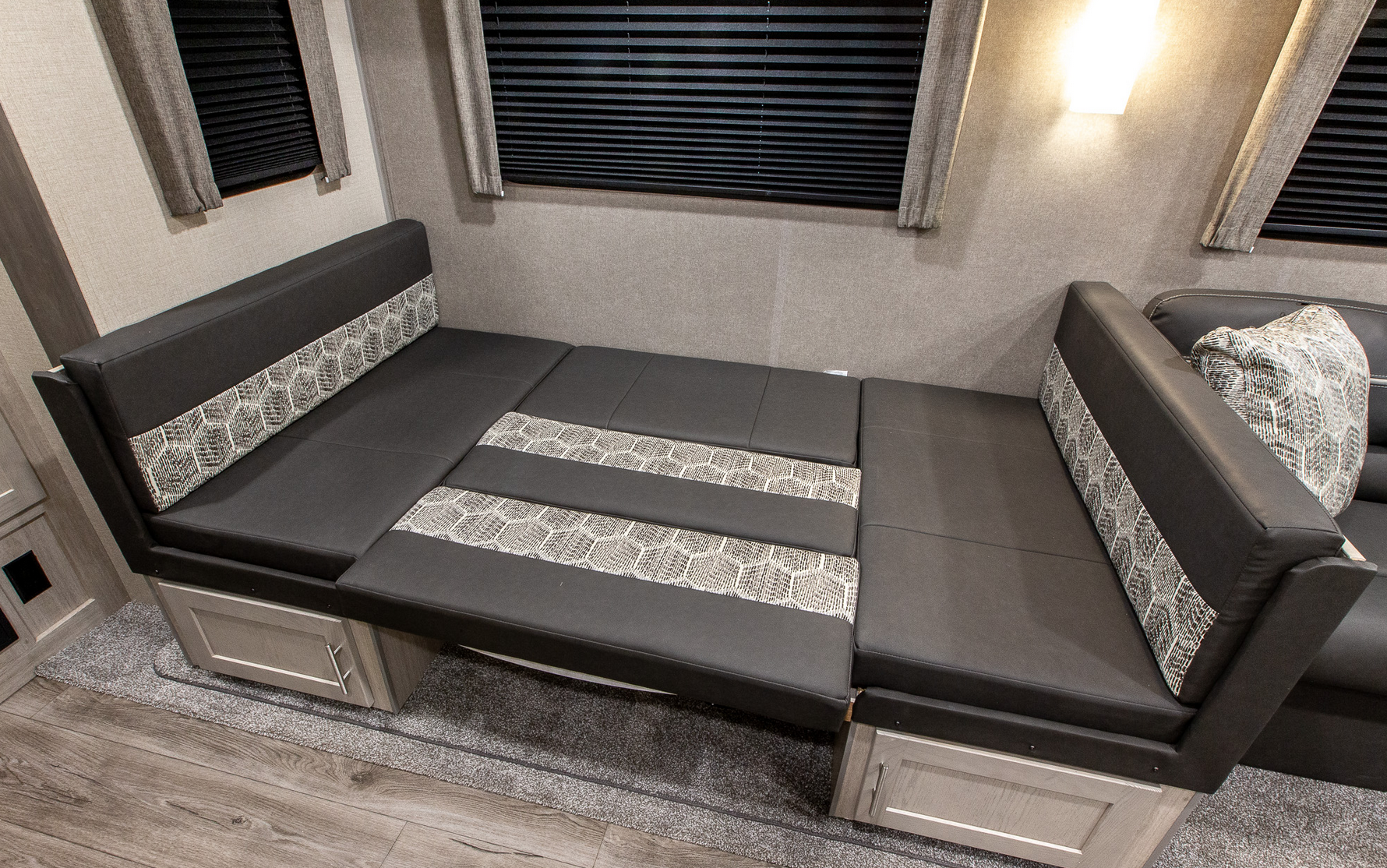 An RV rental's dinette converts to a bed, showing dark gray seating with patterned accents and under-bench storage.. Coachmen Catalina 2022