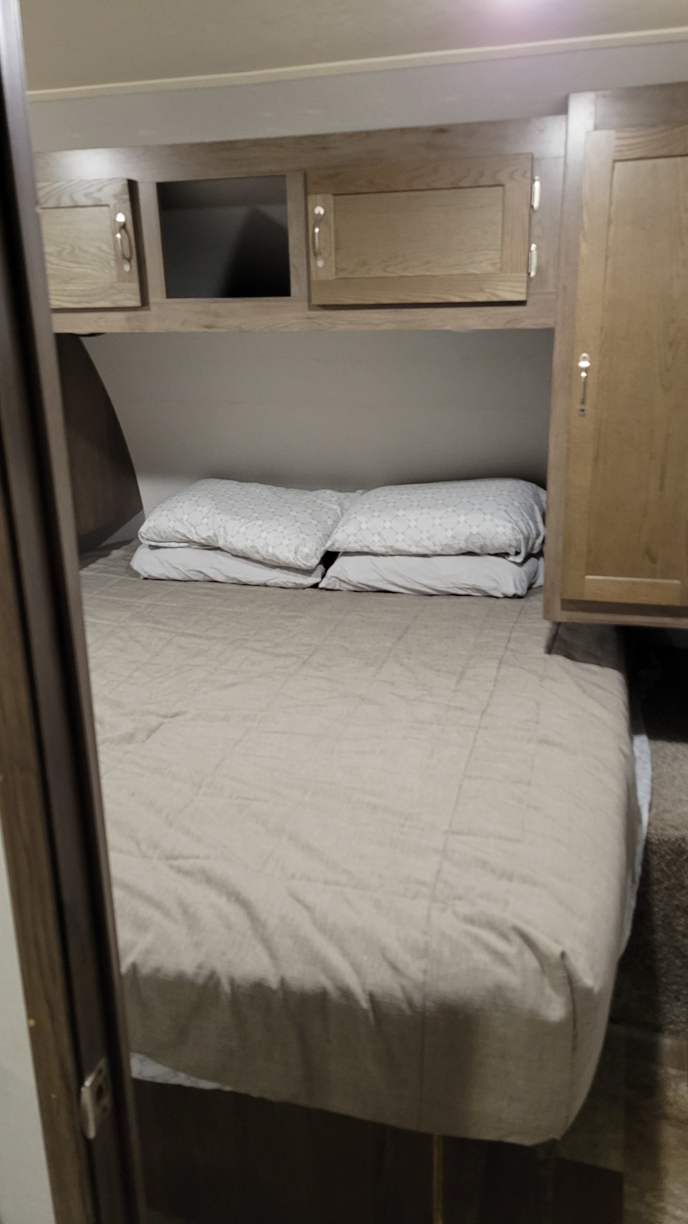 Cozy RV rental bedroom with a comfortable bed, pillows, and practical overhead storage. Ideal for a relaxing night on your adventure.. East to West Silver Lake 2020