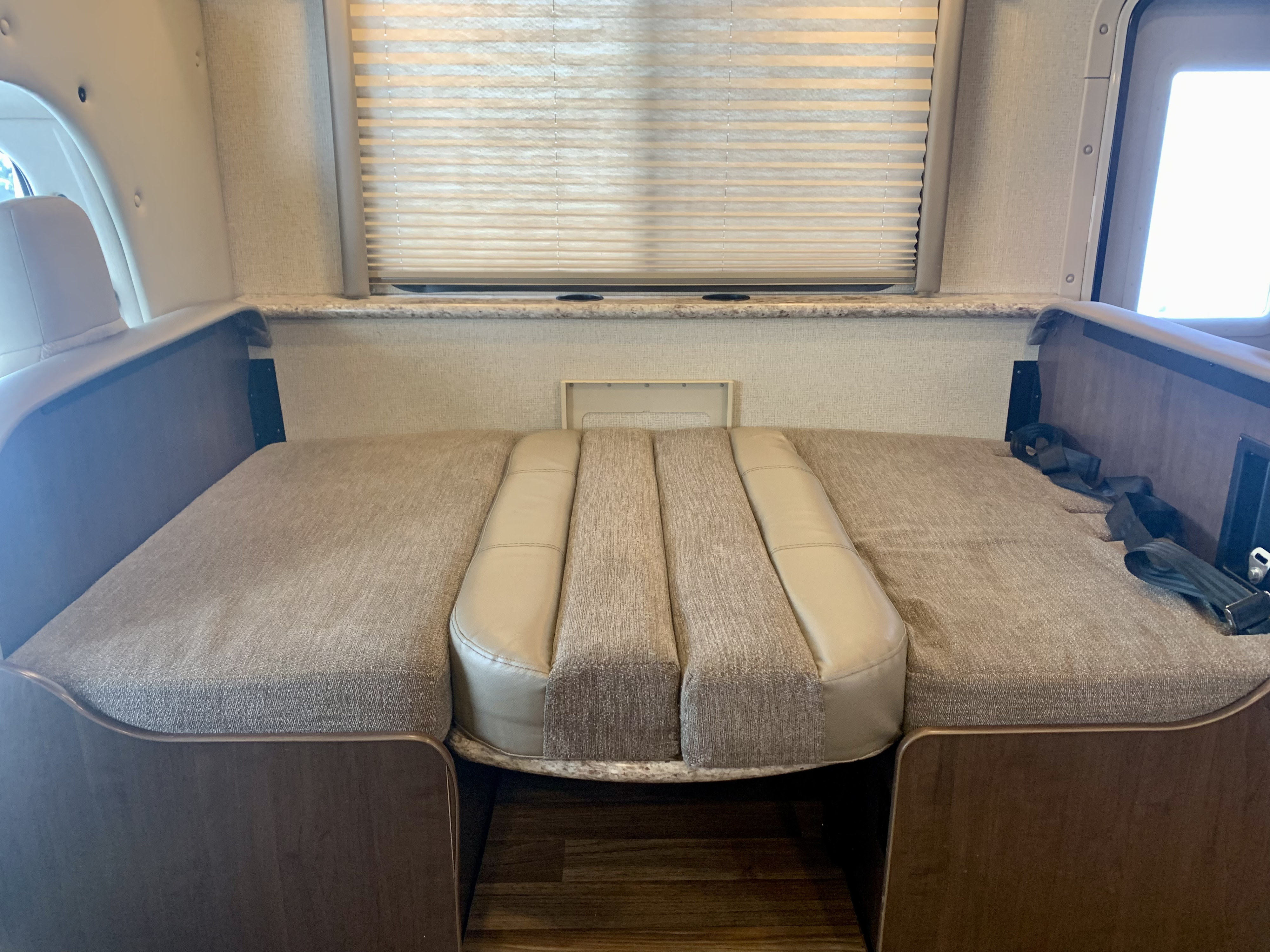 Inside an RV rental: a comfortable dinette bed setup with neutral-toned cushions & window blinds.. Thor Motor Coach Four Winds 2019