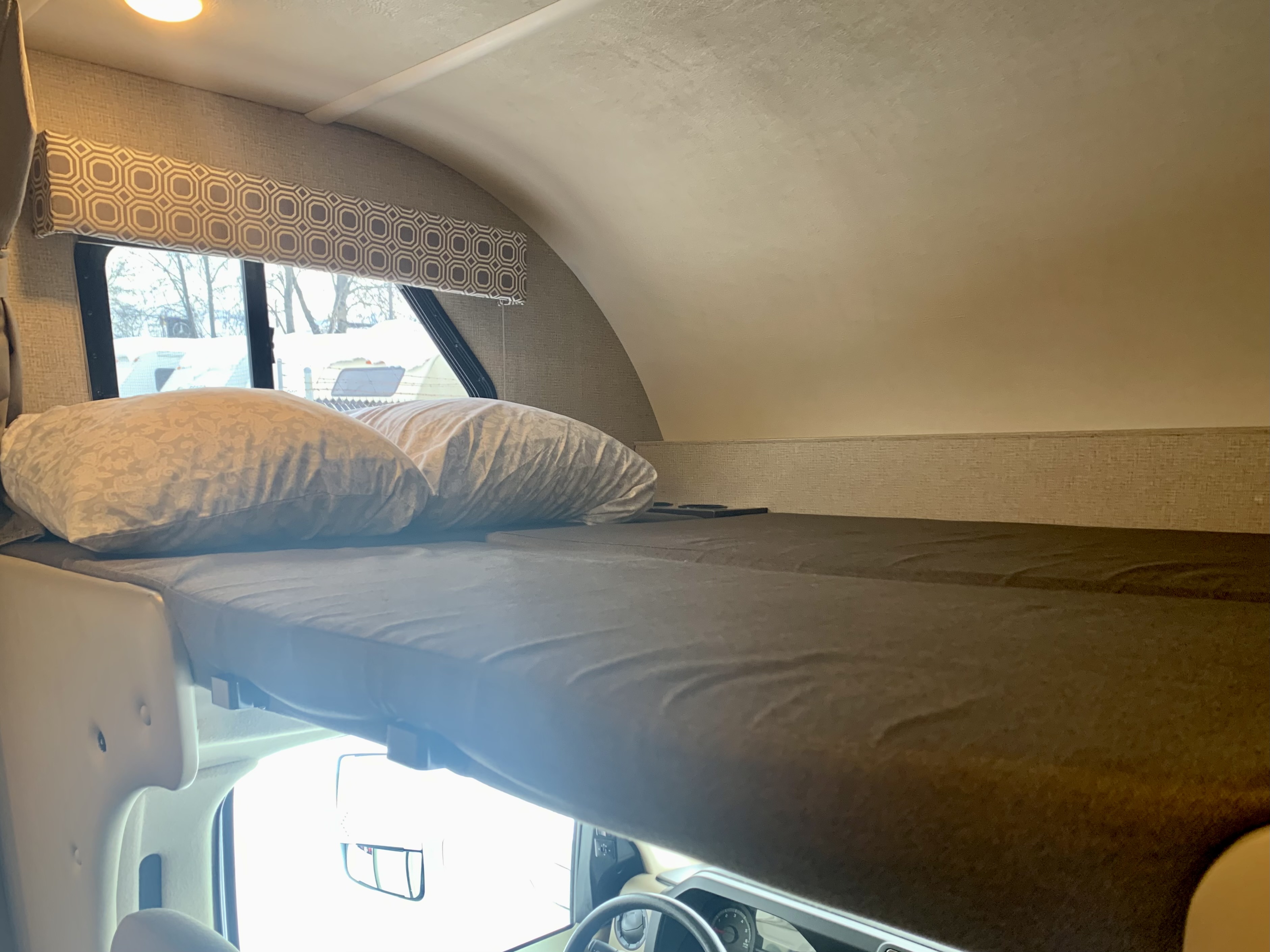 Experience comfort in this RV rental overhead bunk, a cozy sleeping area above the driver's cabin with a window.. Thor Motor Coach Four Winds 2019