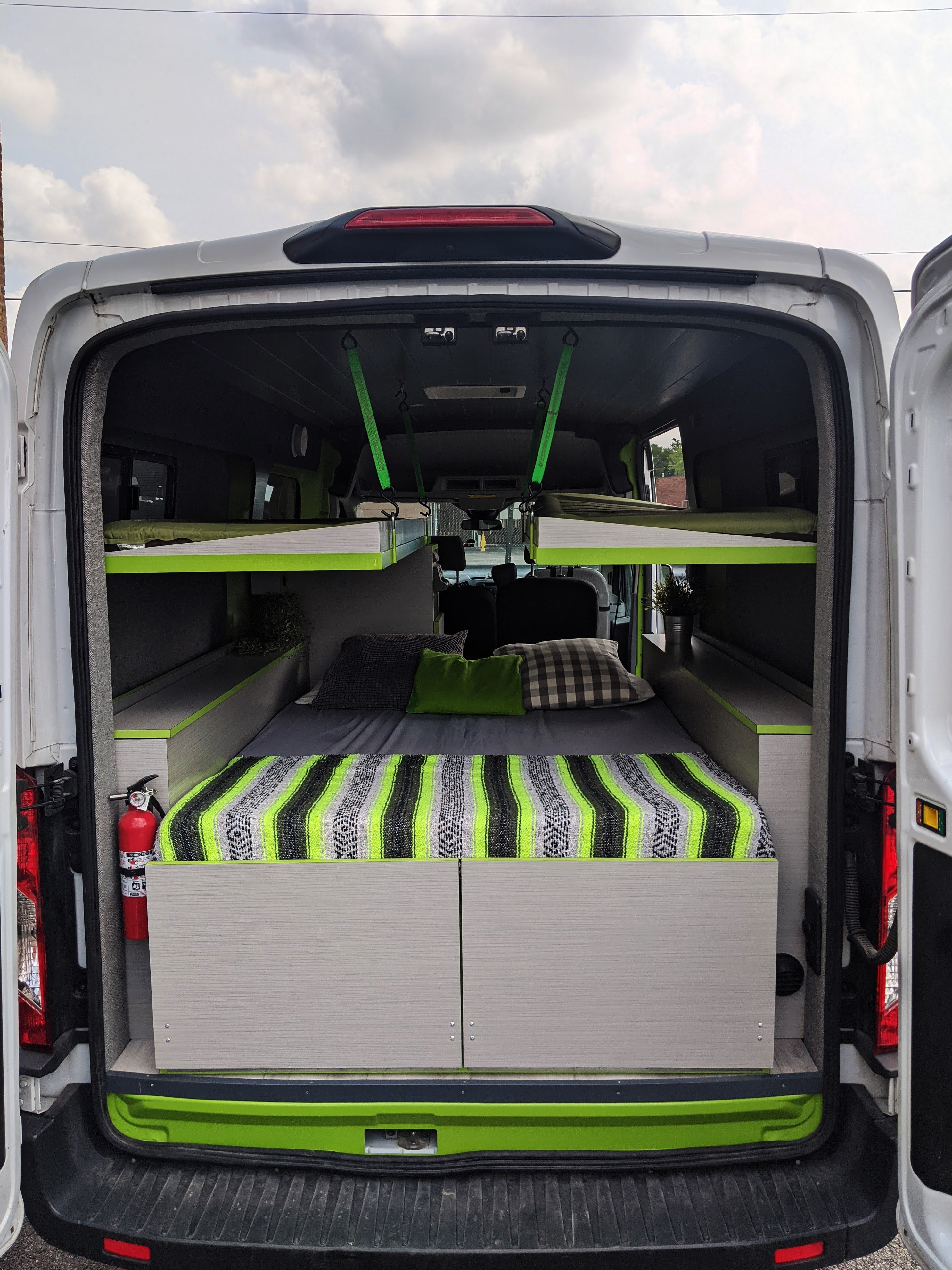 Rear view of a camper van conversion, ideal for an rv rental. Shows a comfortable bed, upper bunk beds, and bright green accents.. Ford Transit 2018