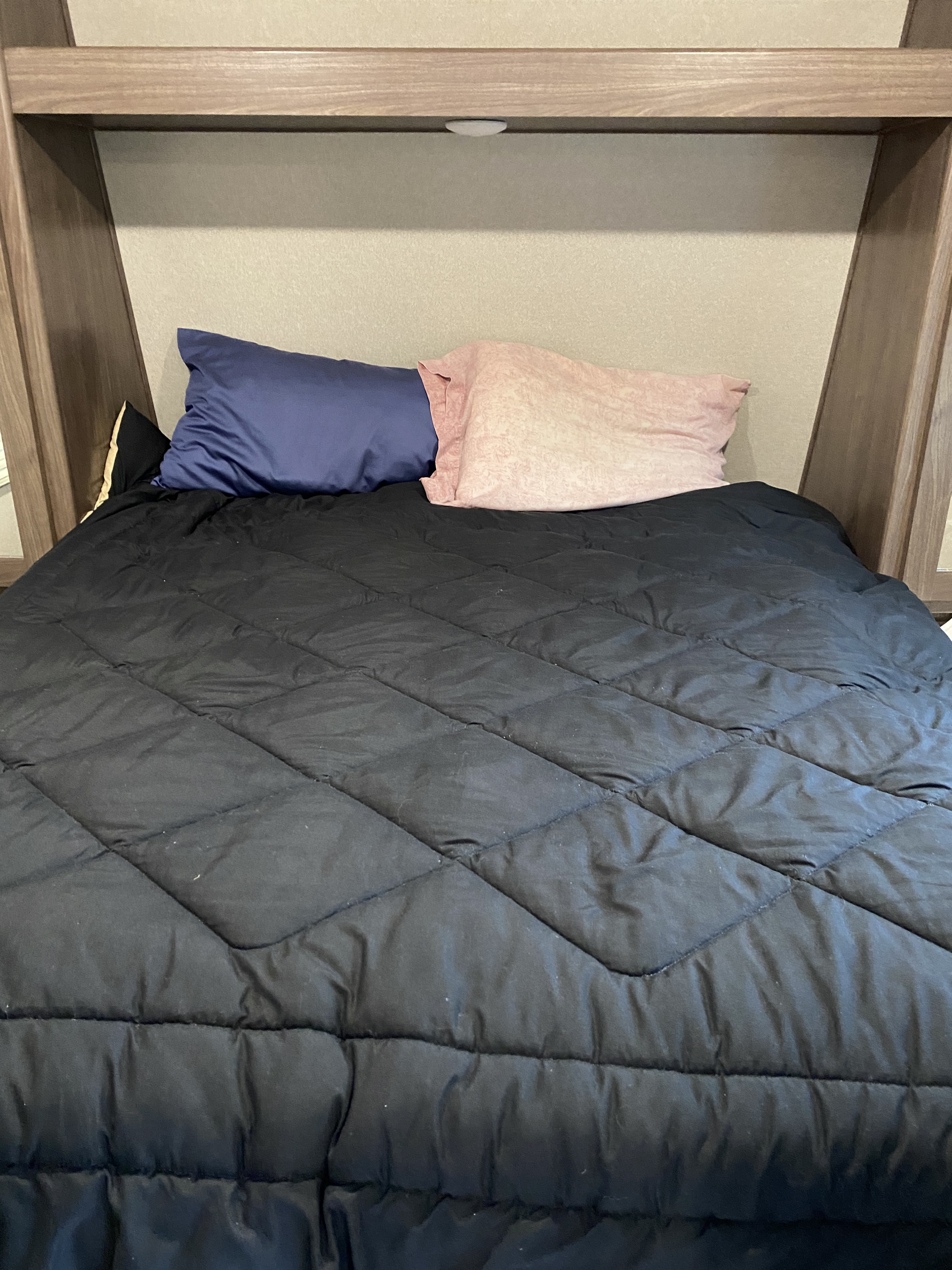 Comfortable bed in an RV rental bedroom. A black comforter and two pillows are visible, set within the compact interior space.. Keystone RV Hideout Luxury 2019
