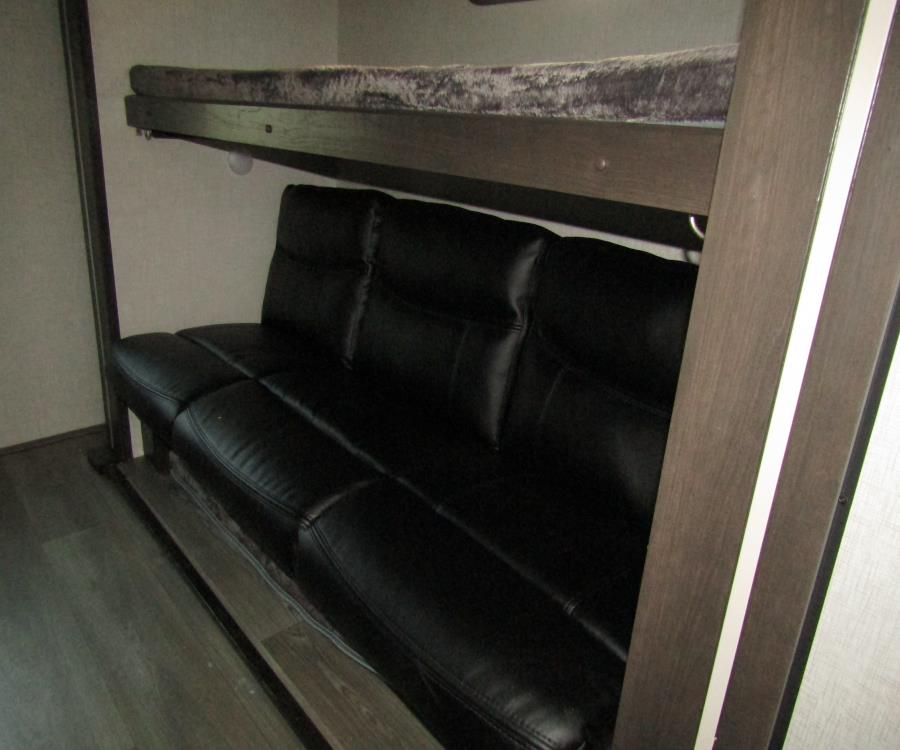 RV rental bunkhouse: A black sofa sits below a bunk bed, maximizing sleeping and seating capacity in this compact interior.. keystone cruiser aire-tt 2022