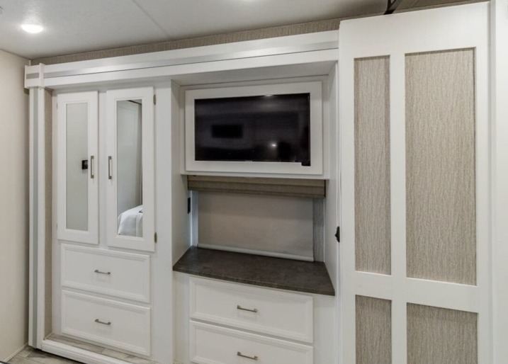Modern RV rental interior showing a bedroom wardrobe with mirrored doors, TV, and integrated storage cabinets.. Coachmen Encore 2022