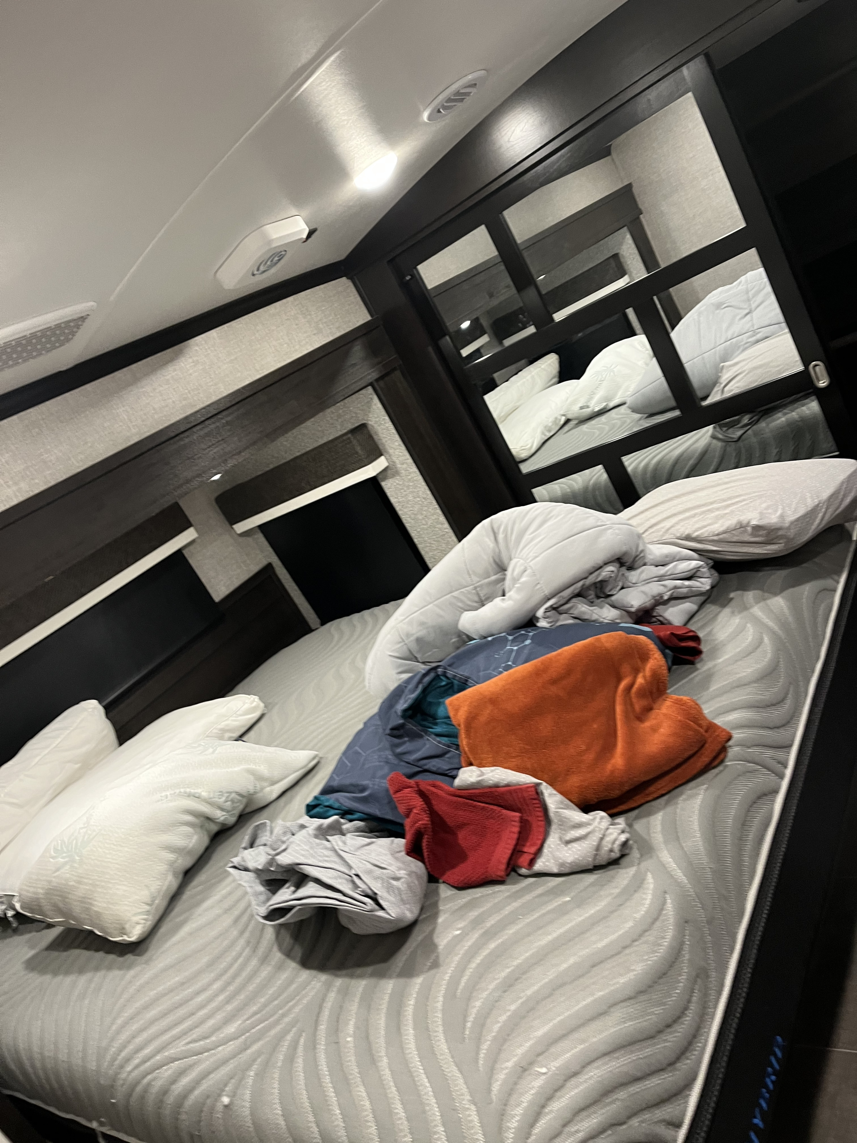 An RV rental bedroom features an unmade bed with pillows and clothes, reflecting bunk beds in the mirrors.. Jayco North Point 2022