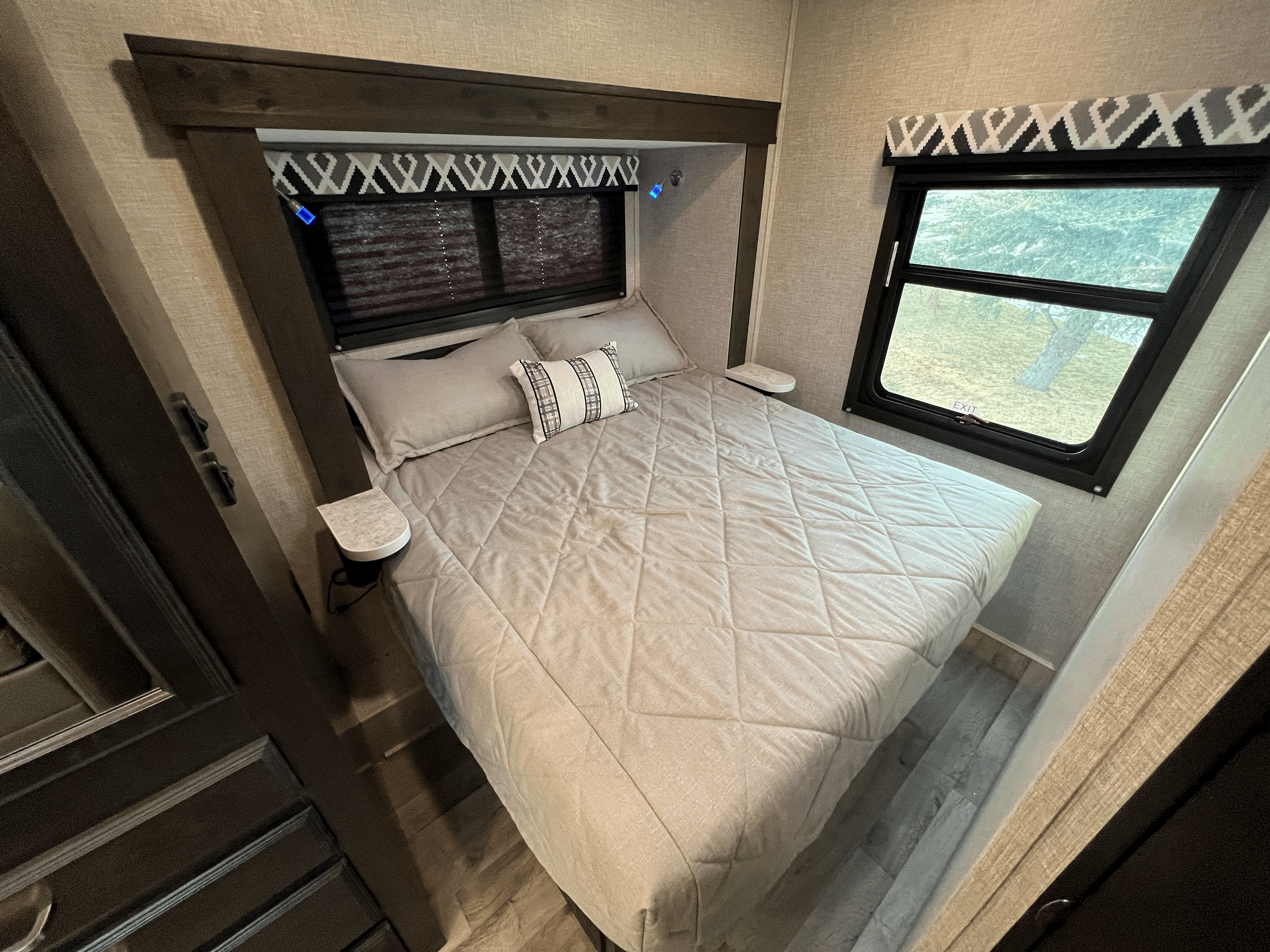 Serene RV rental bedroom with neutral-toned bed, blue reading lights, and a window offering a view of the outdoors.. Jayco 26XD REDHAWK 2022