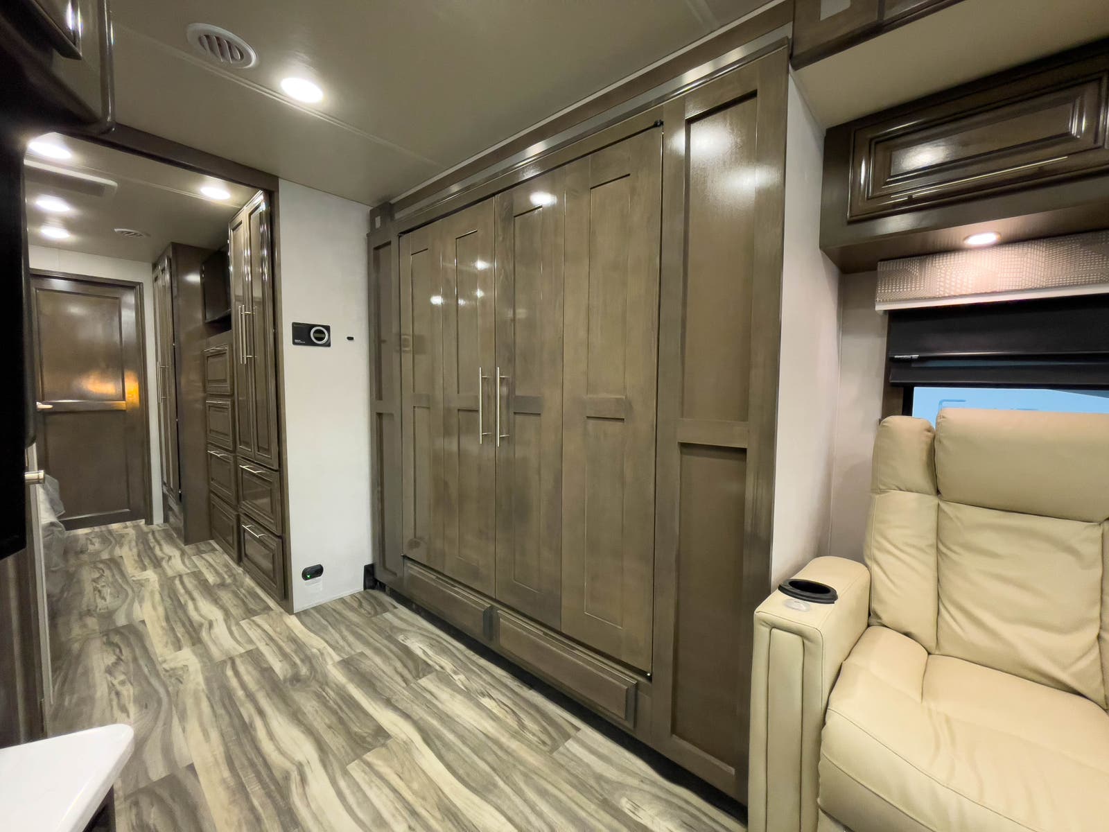 Inside an RV rental: neutral wood-look flooring, sleek wood cabinetry/murphy bed, and a comfortable light recliner with a cup holder.. Forest River Georgetown 2022