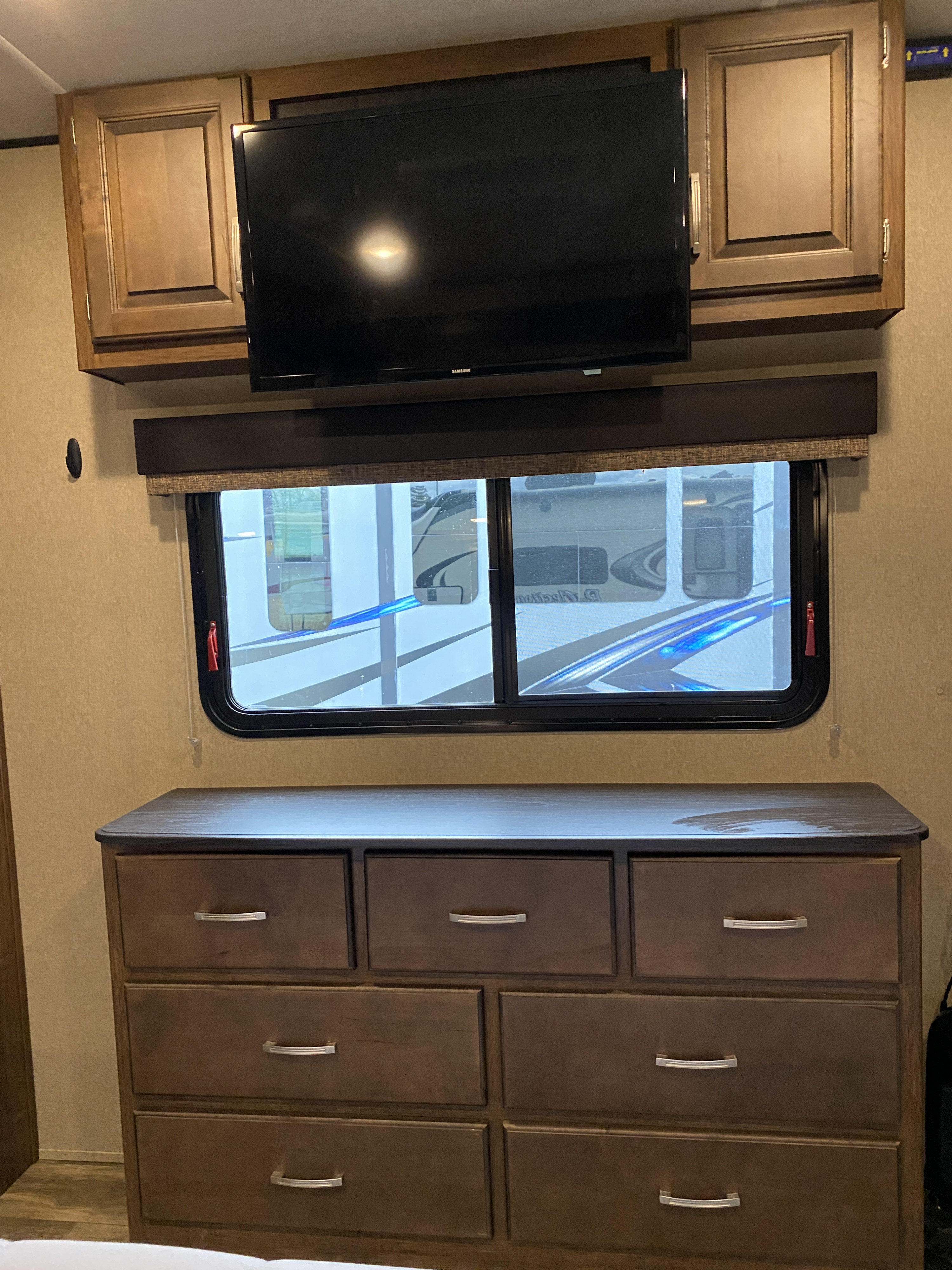 RV rental interior featuring a wall-mounted TV, window, and wood-toned dresser with silver pulls.. Grand Design Reflection 2019