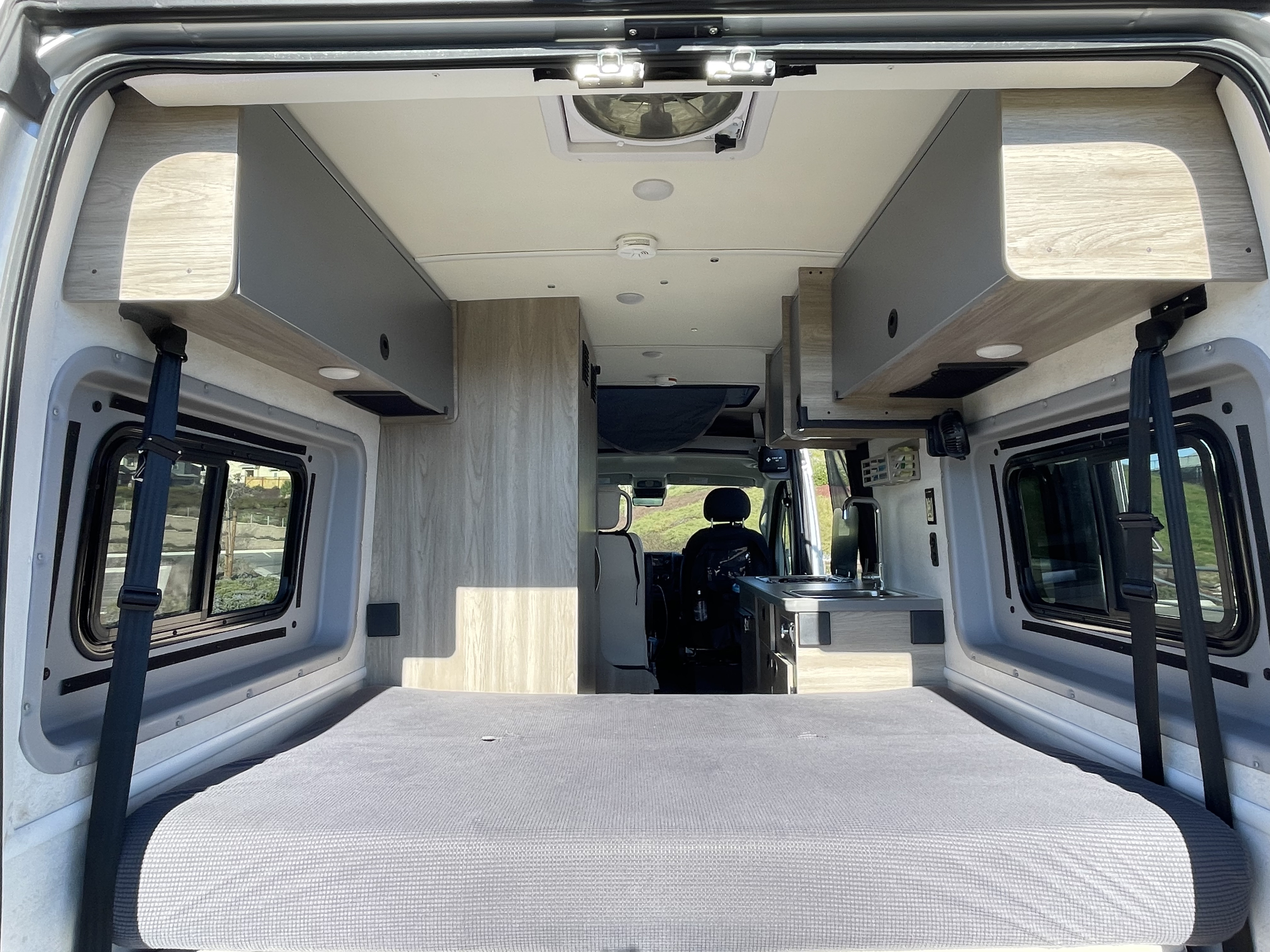 Spacious RV rental interior with a comfortable bed, side windows, overhead storage, and a full kitchen.. Winnebago Solis 2022