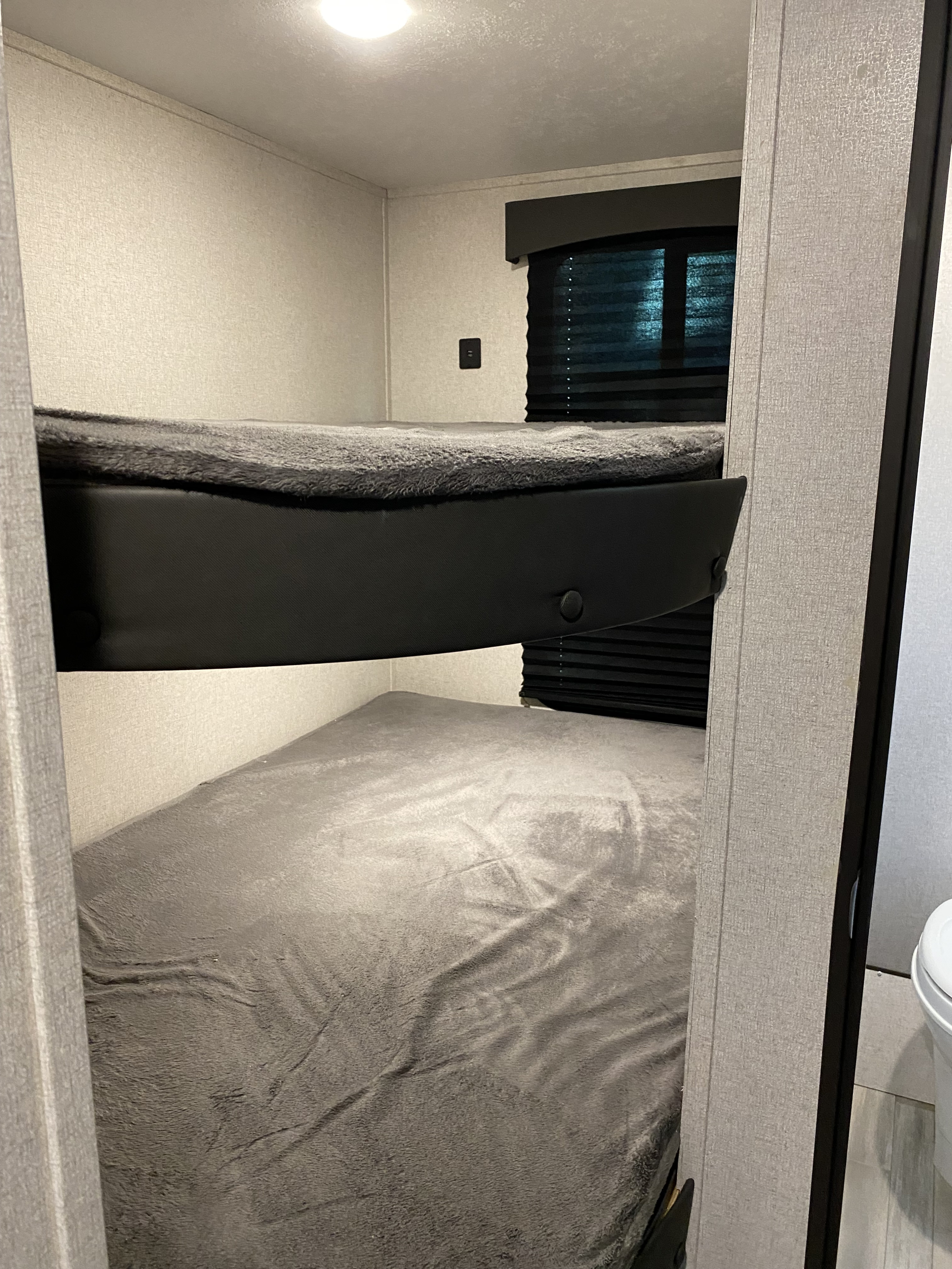 Cozy RV rental interior showing two bunk beds with grey blankets. Features a window with blinds & USB port.. Clipper Other 2021