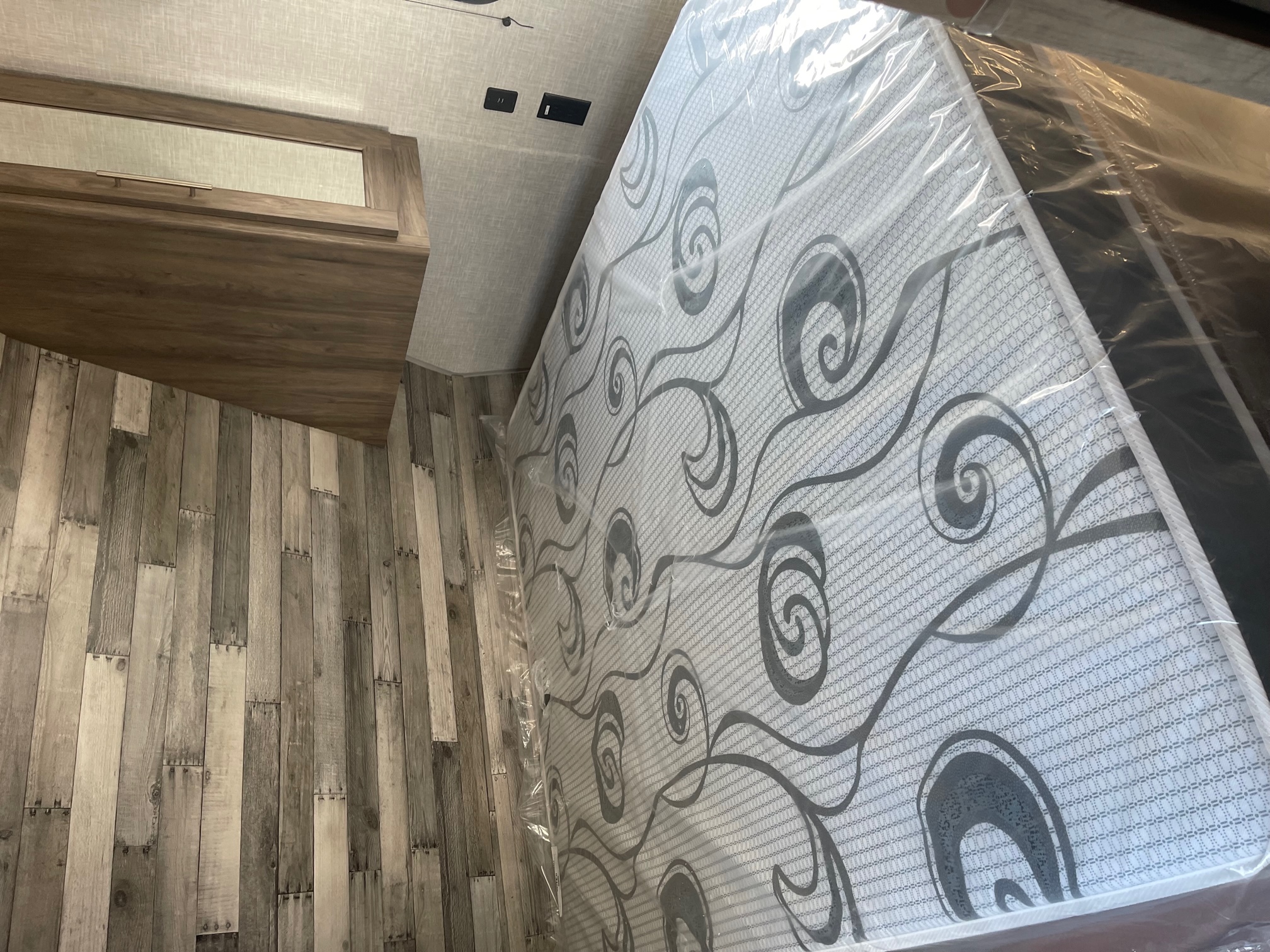 Spacious RV rental bedroom featuring a new mattress in plastic, rustic wood paneling, and overhead storage.. Zinger Crossroads ZR280BH22 2022