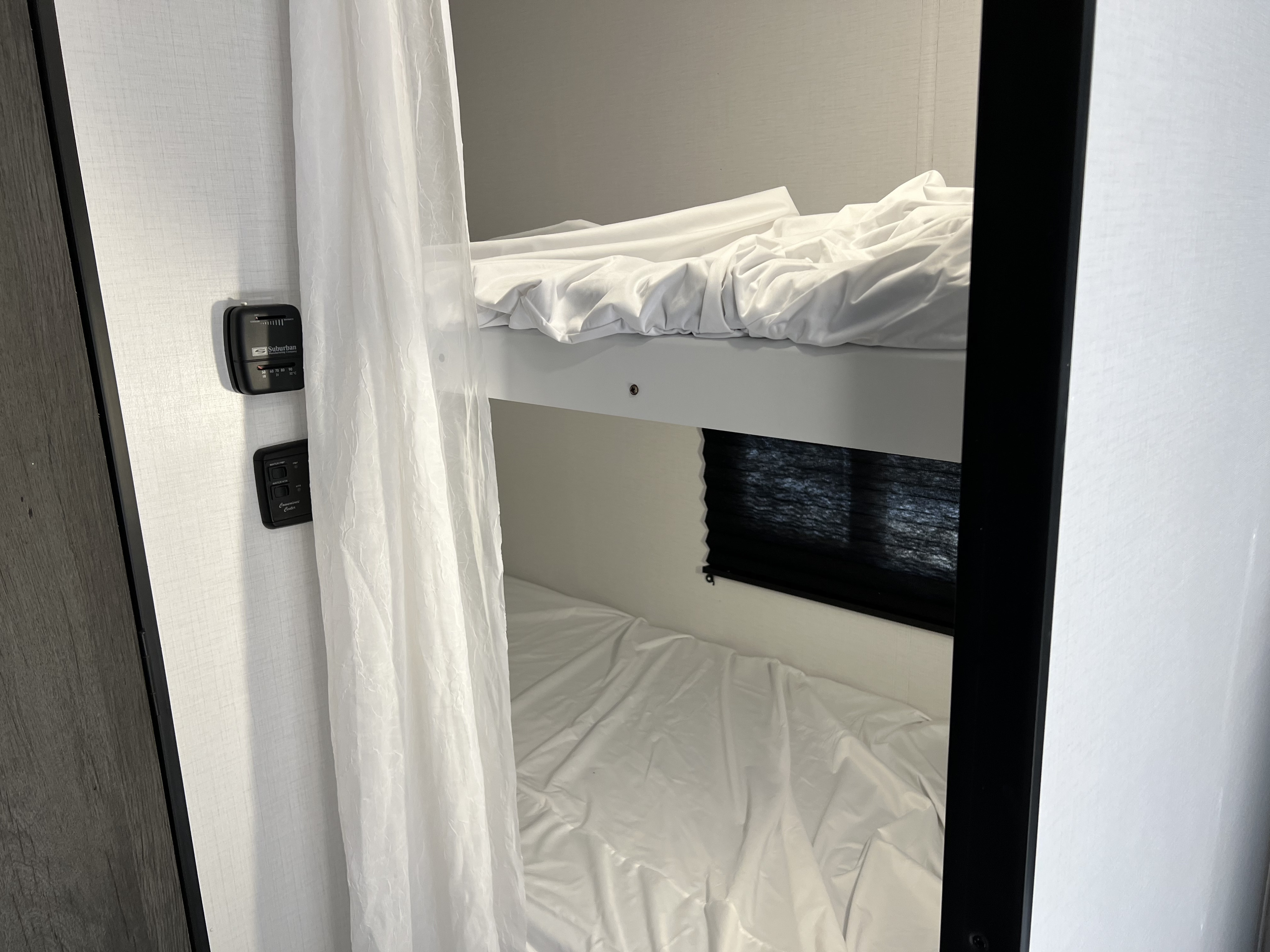 An RV rental's sleeping area features two bunk beds with white sheets. Control panels are visible on the wall.. Keystone RV Hideout LHS 176 2021