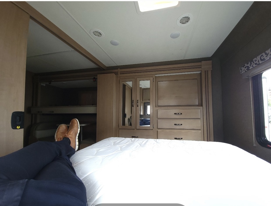 Inside an RV rental, a person's feet rest on the bed. Bunk beds, wardrobe, and ceiling details are visible.. Thor Four Winds 2020