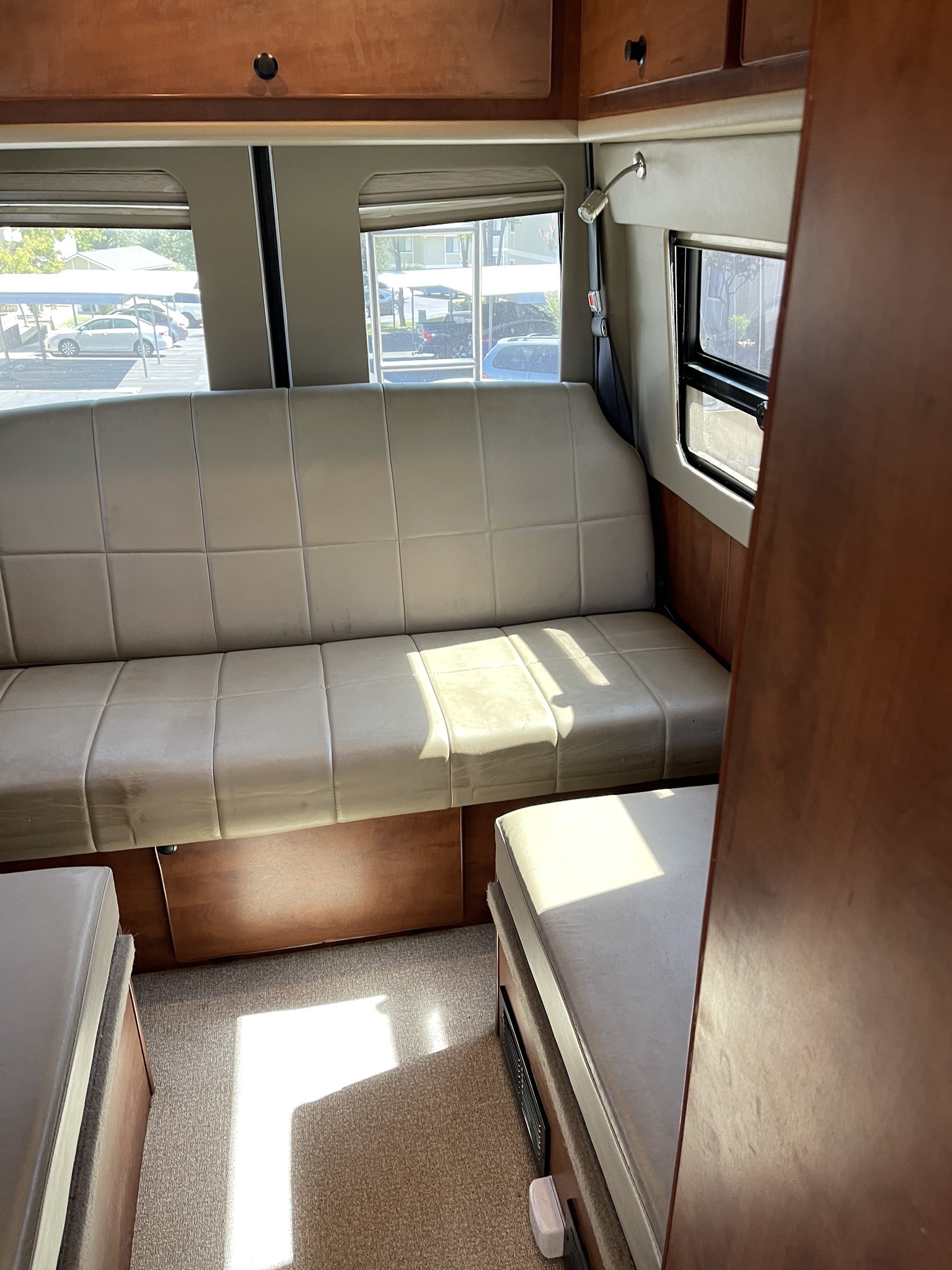 Inside an RV rental: light-colored bench seating, wood cabinets, and large windows revealing the outside.. Sportsmobile Custom Design 2013