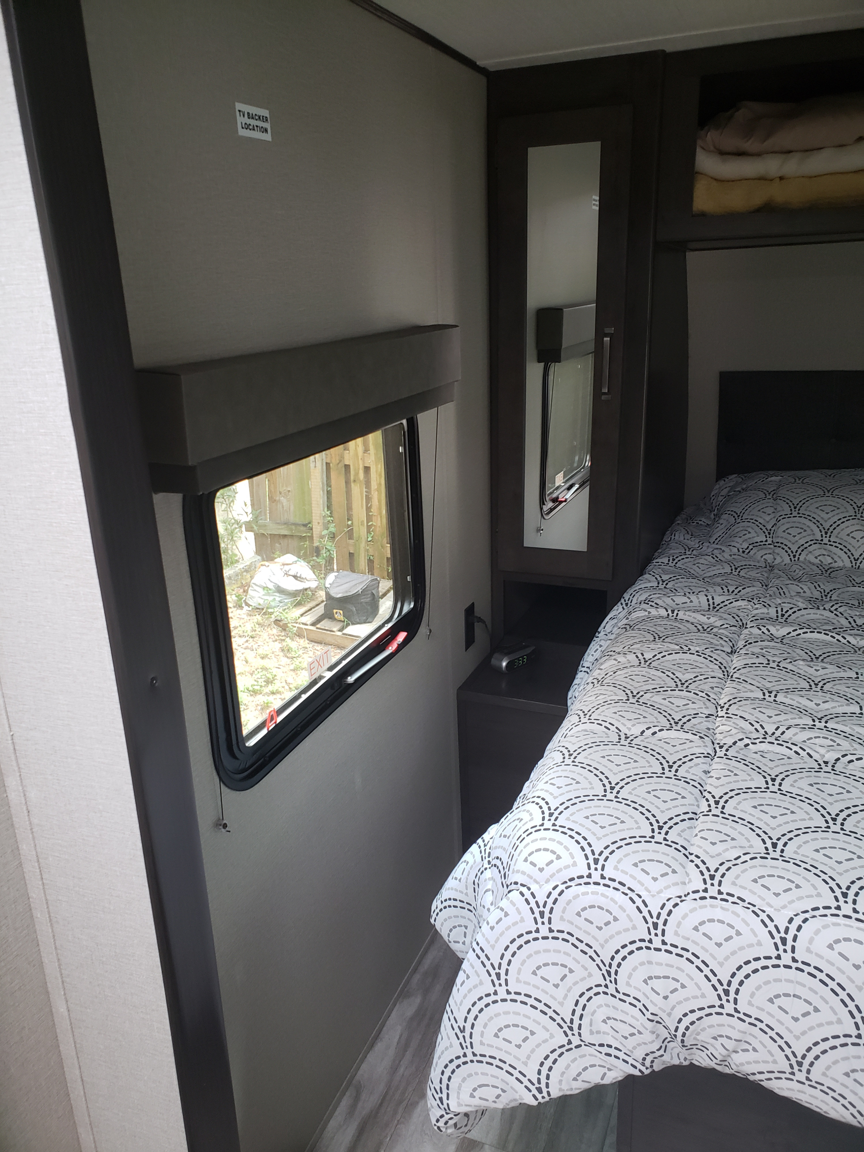 Cozy RV rental bedroom: patterned bed, window, nightstand with clock, and built-in storage, ideal for road trips.. Grand Design Transcend Xplor 2022