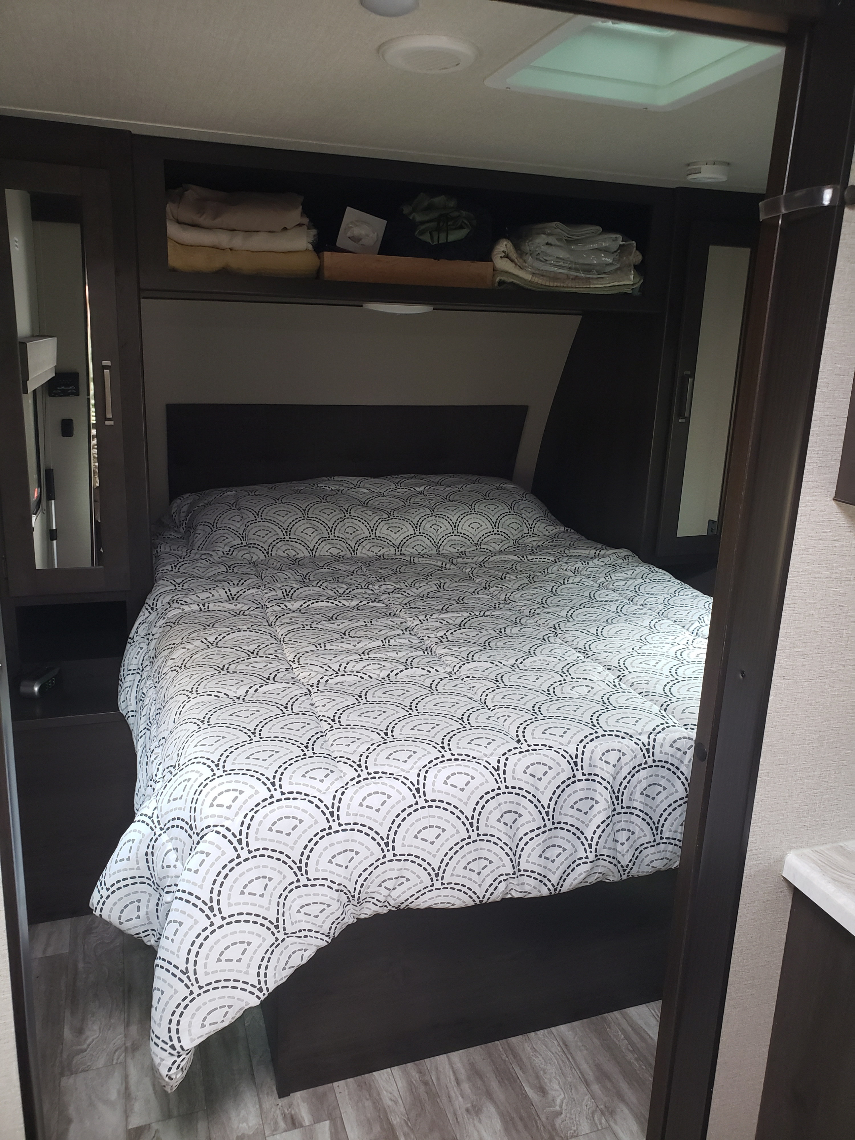 Inside an RV rental, a bed with a modern patterned comforter and smart storage solutions for travelers.. Grand Design Transcend Xplor 2022