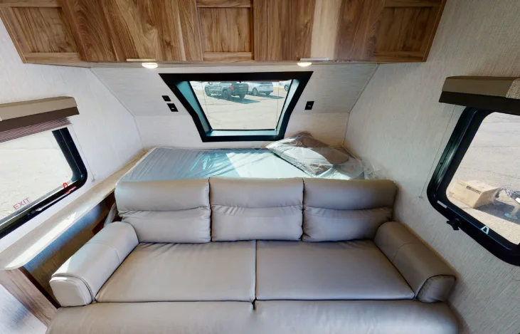 Inside an RV rental: a comfy grey sofa, a bed with a large window, and wooden cabinets for a cozy space.. Forest River Palomino Palomini 2021