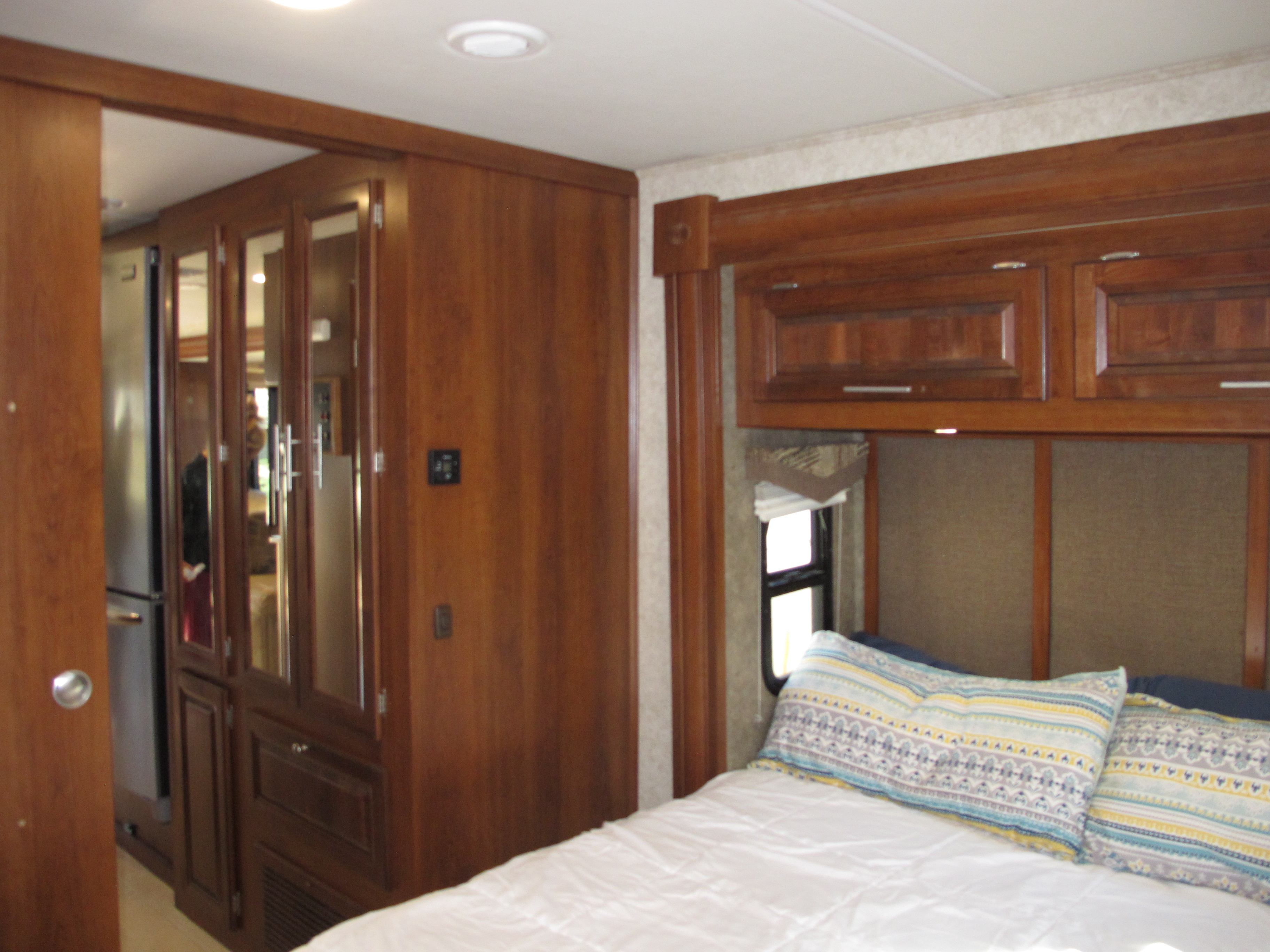 Interior of an RV rental: a cozy bedroom with wood cabinetry, a bed, and a mirrored closet leading to the kitchen area.. Georgetown XL 2015