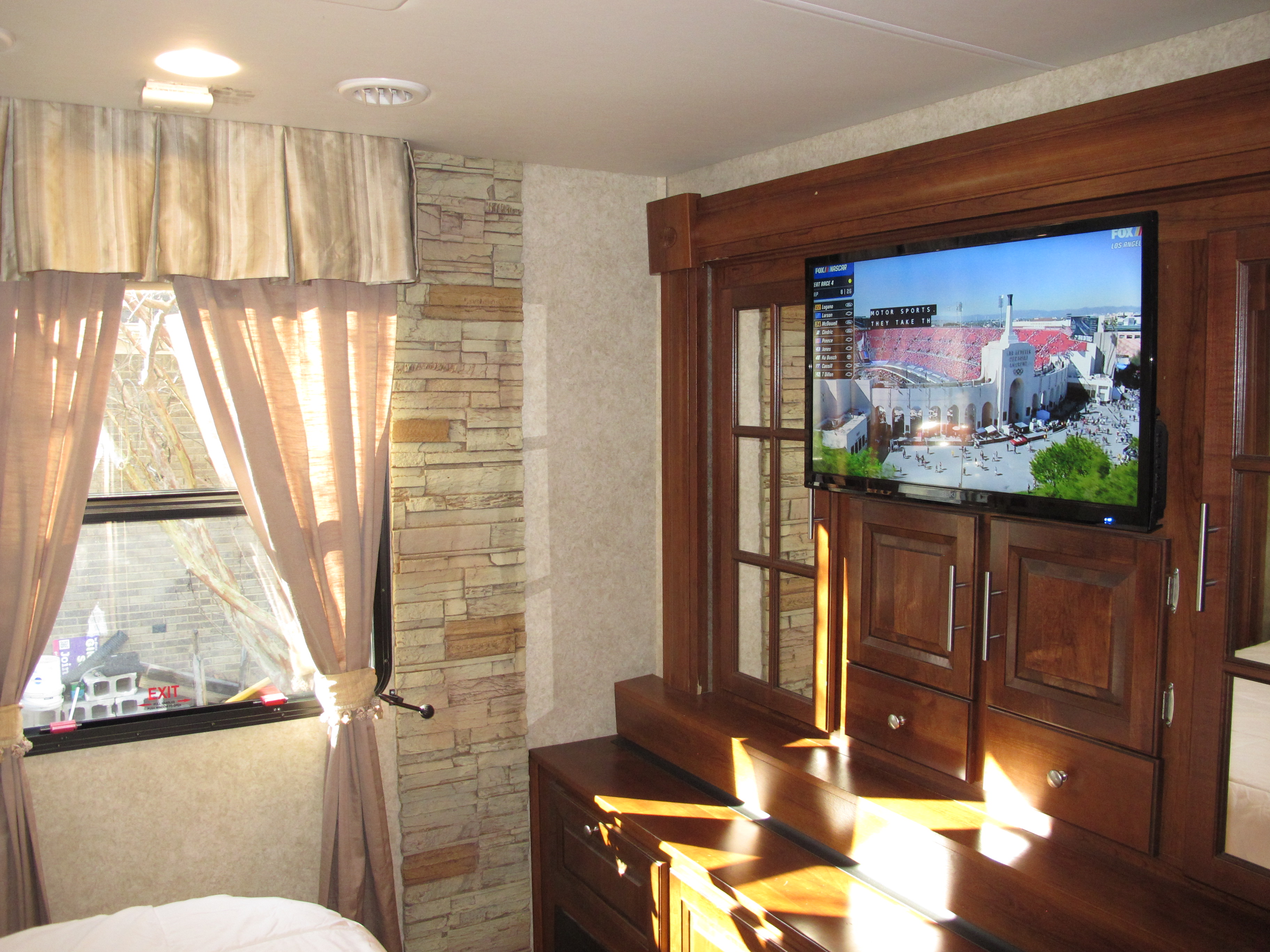 Cozy RV rental interior featuring a TV playing NASCAR, window with curtains, and elegant wood furnishings.. Georgetown XL 2015