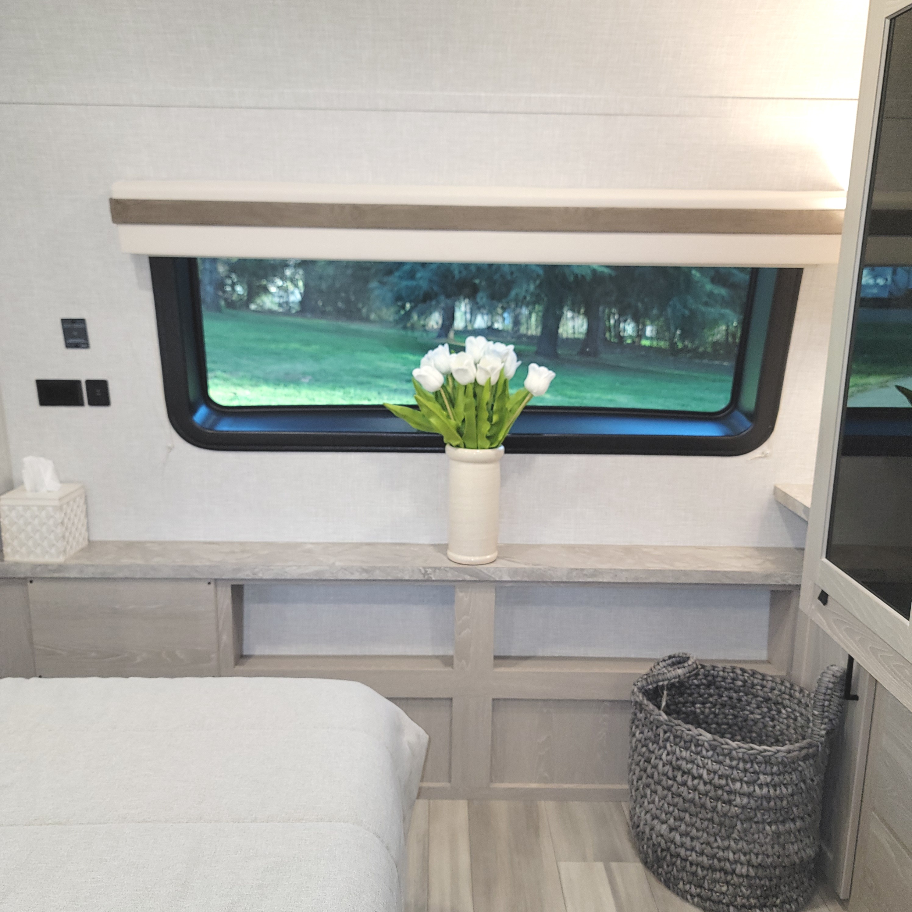 Relaxing RV rental bedroom with a bed, modern shelf, white tulips, and a window framing lush green nature views.. Forest River Rockwood 2022