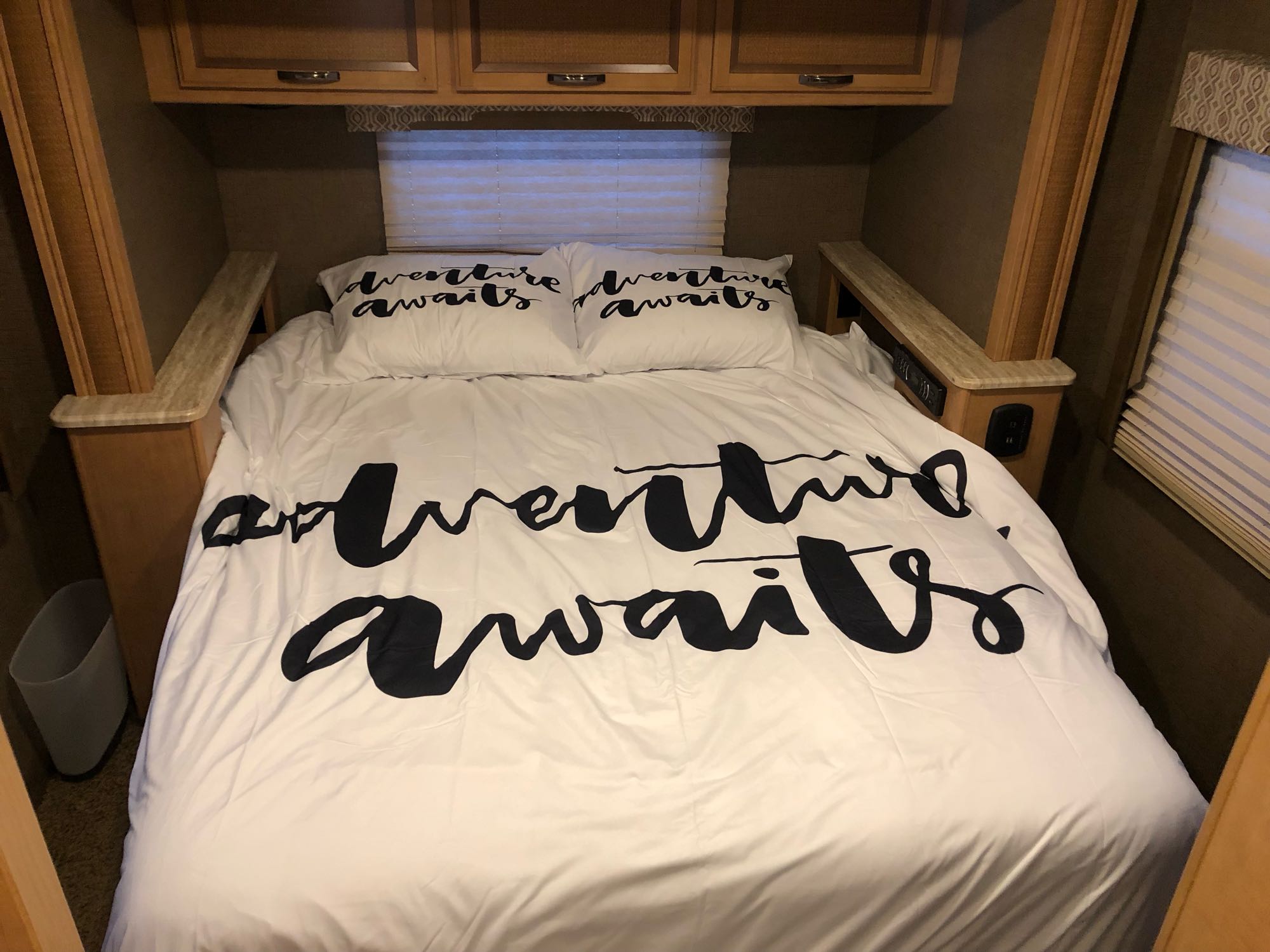 Cozy RV rental bedroom. White bedding reads 'adventure awaits' with overhead cabinets & side shelves, great for travel.. Thor Vegas 2017