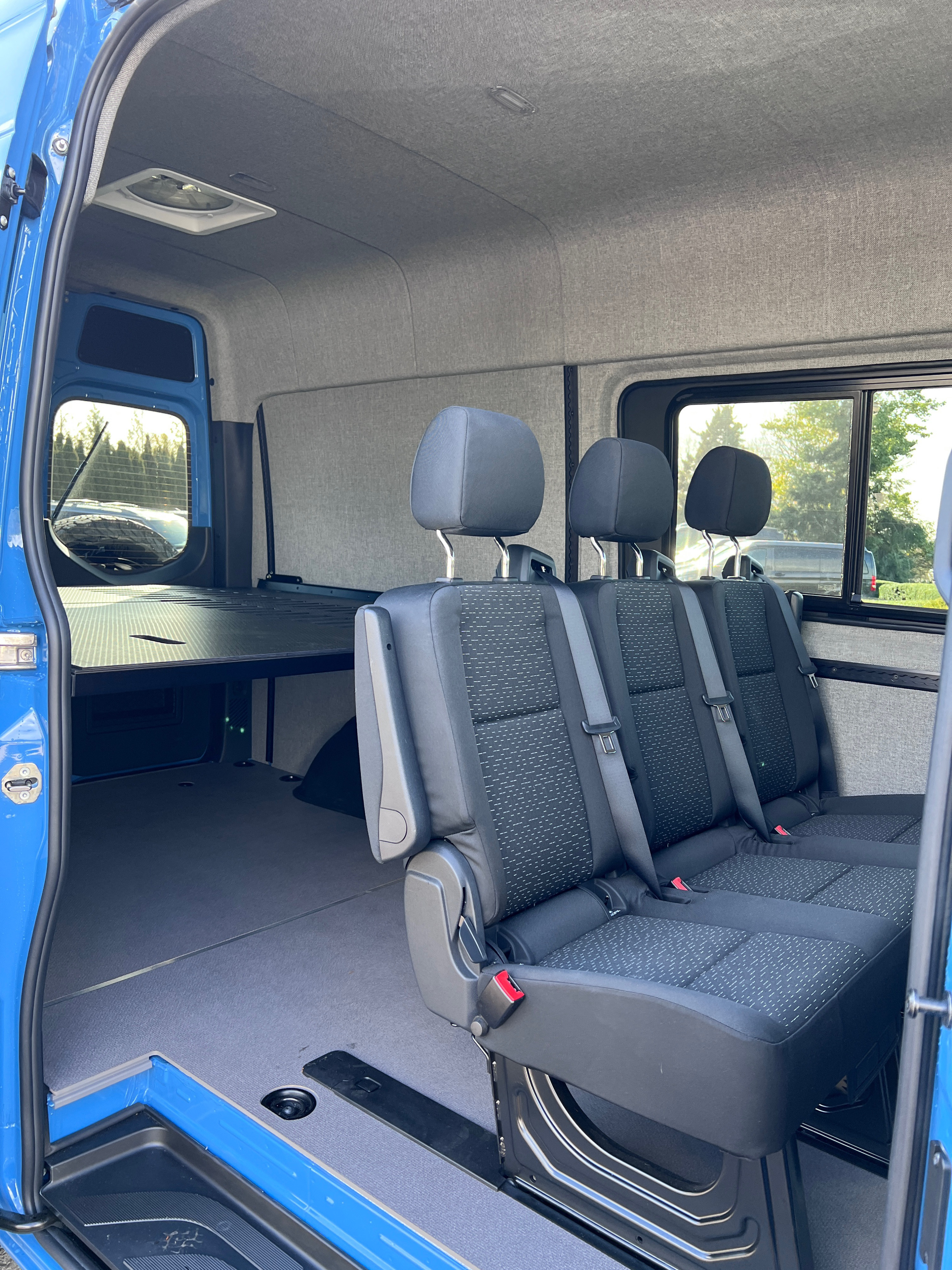 Spacious RV rental van interior with comfortable passenger seating, a raised bed/storage platform, and soft upholstered walls.. Mercedes-Benz Sprinter 2021