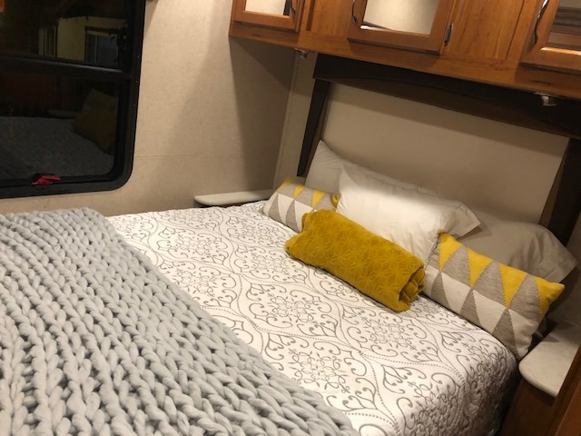 Cozy RV rental bedroom with patterned bedding, yellow accents, and chunky knit blanket.. Jayco Greyhawk 2016