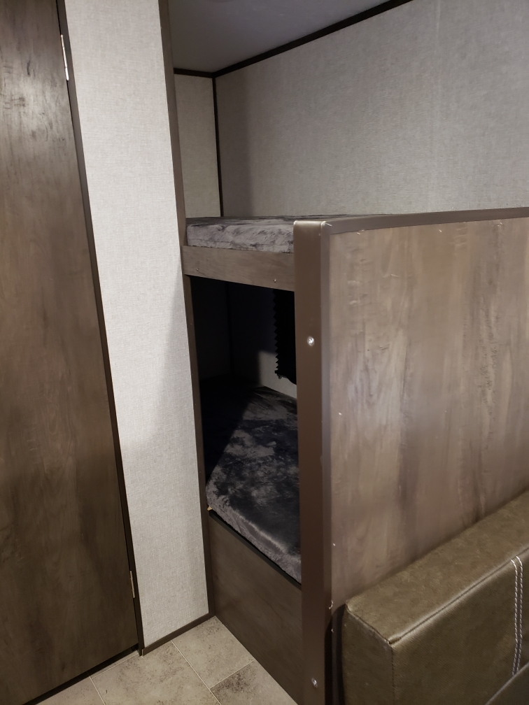 Cozy bunk beds with dark cushions in an RV rental interior, showcasing compact sleeping space and wood-toned finishes.. Dutchmen Coleman Lantern LT 2022