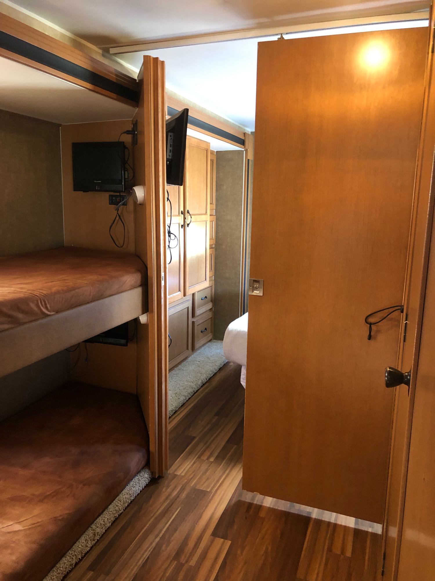 Inside an RV rental, showing bunk beds with TVs, wood flooring, and a partially open door to a private bedroom.. Coachmen Freelander 2014