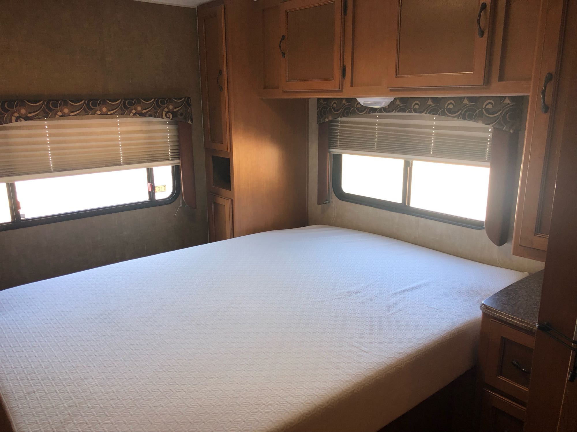 Inside an RV rental: cozy bedroom featuring a comfortable white bed, windows with blinds, and storage cabinets.. Coachmen Freelander 2014