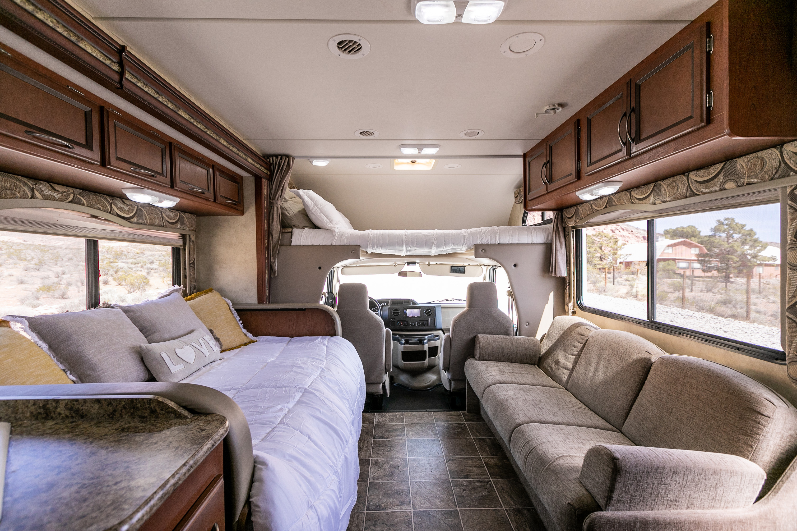 Spacious RV rental interior featuring a cozy bed, comfortable sofa, and overhead bunk.. Thor Four Winds 2013