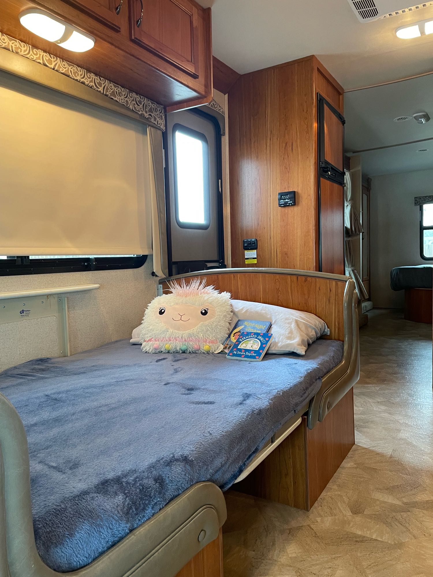 Bright RV rental interior: a child's bed with a llama plushie & books, facing a kitchen area and rear bunk.. Jayco Redhawk 2016