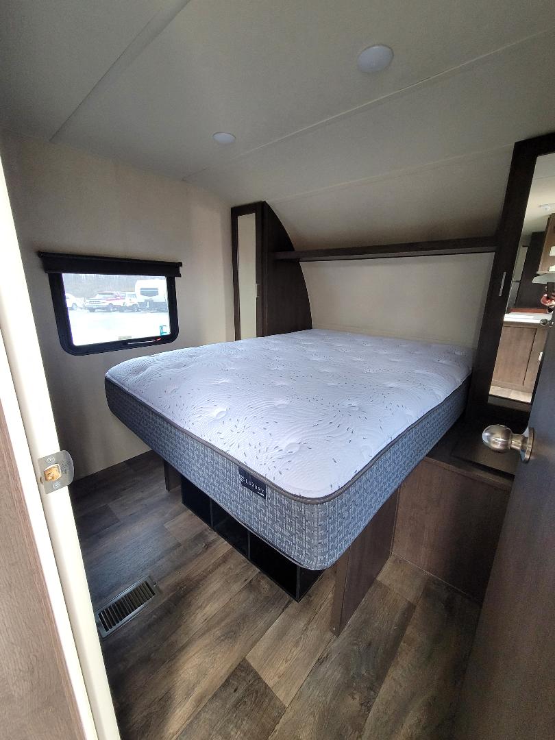 Inside an RV rental bedroom: a comfortable queen bed with a patterned mattress, built-in storage, and a window view.. Forest River Salem 2018