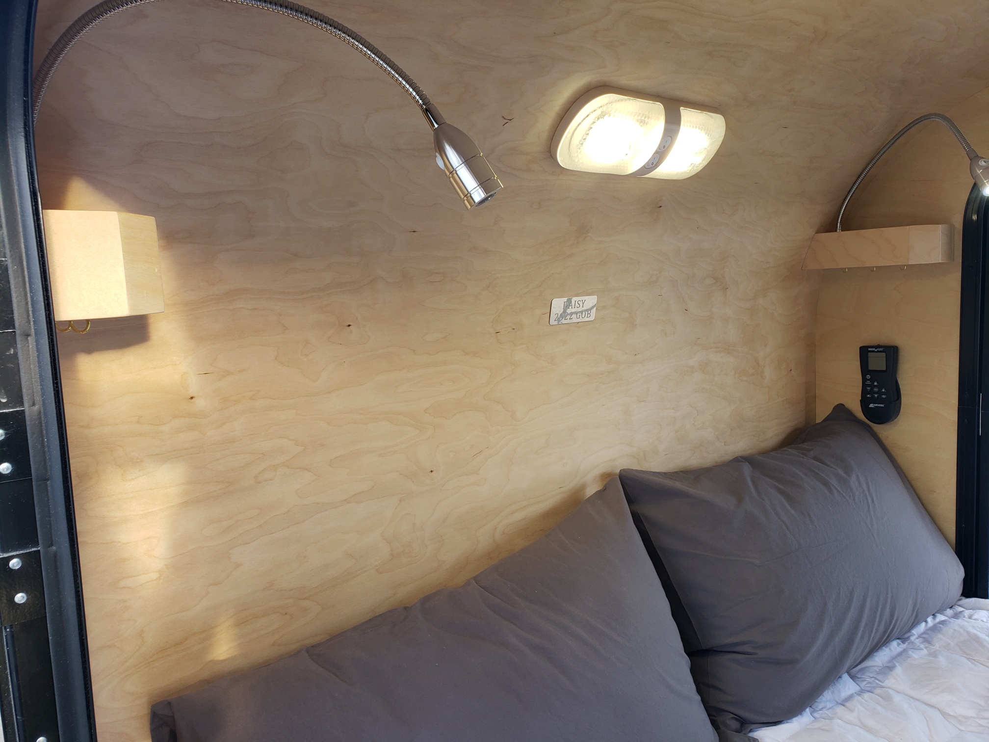 Cozy RV rental sleeping area featuring wood-paneled walls, bright overhead light, reading lamp, and two plush pillows on a bed.. Gnome Home Gnome Home 2022