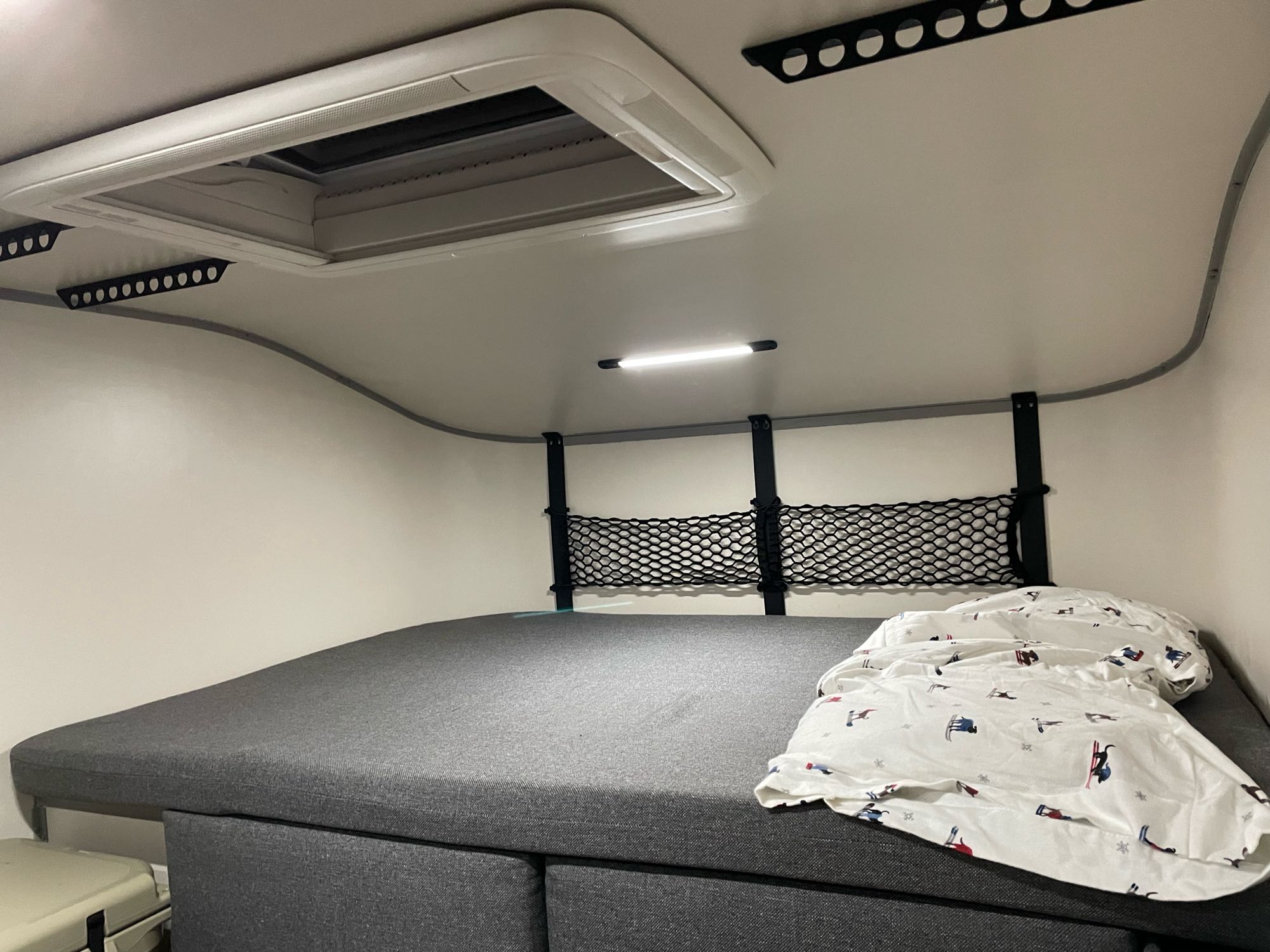 RV rental interior: a comfy bed with ski duvet, skylight, overhead lights, and practical storage netting.. Ford Ranger 2021