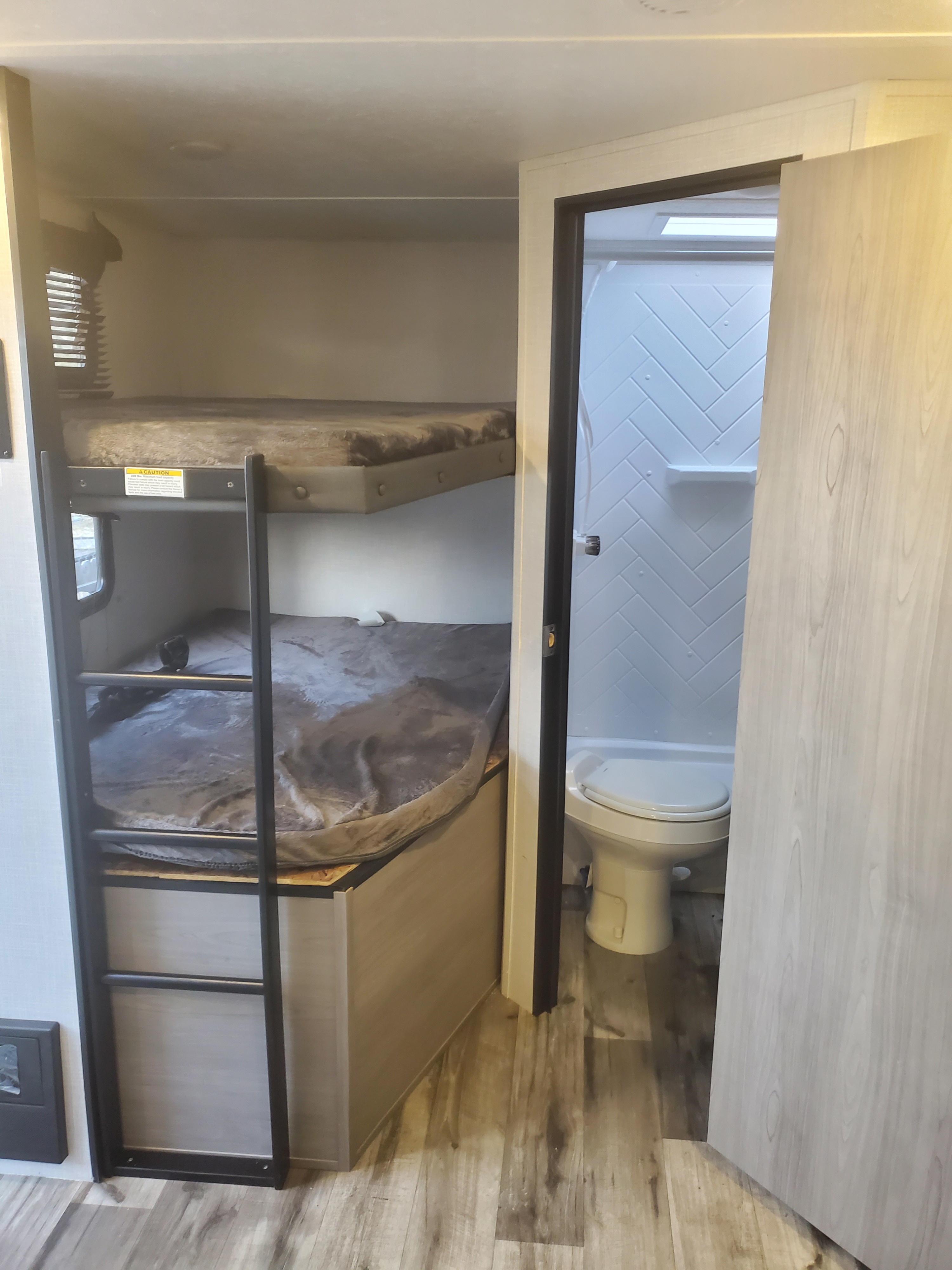 RV rental interior: bunk beds with ladder on left, compact bathroom with toilet and herringbone shower on right.. Coleman 2455bh 2022
