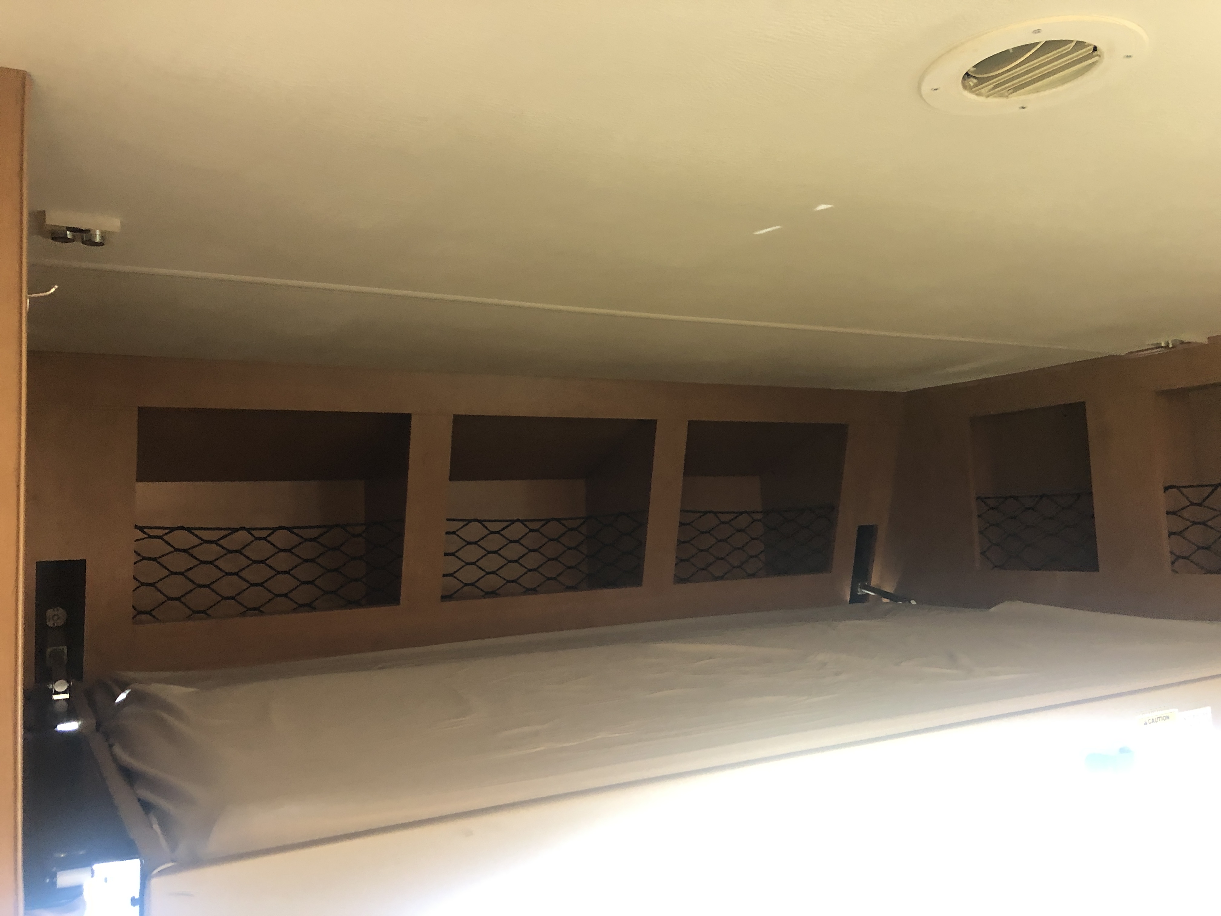 RV rental bedroom with a neatly made bed, overhead storage cubbies with mesh netting, and ceiling air vent.. Thor A.C.E. 2017
