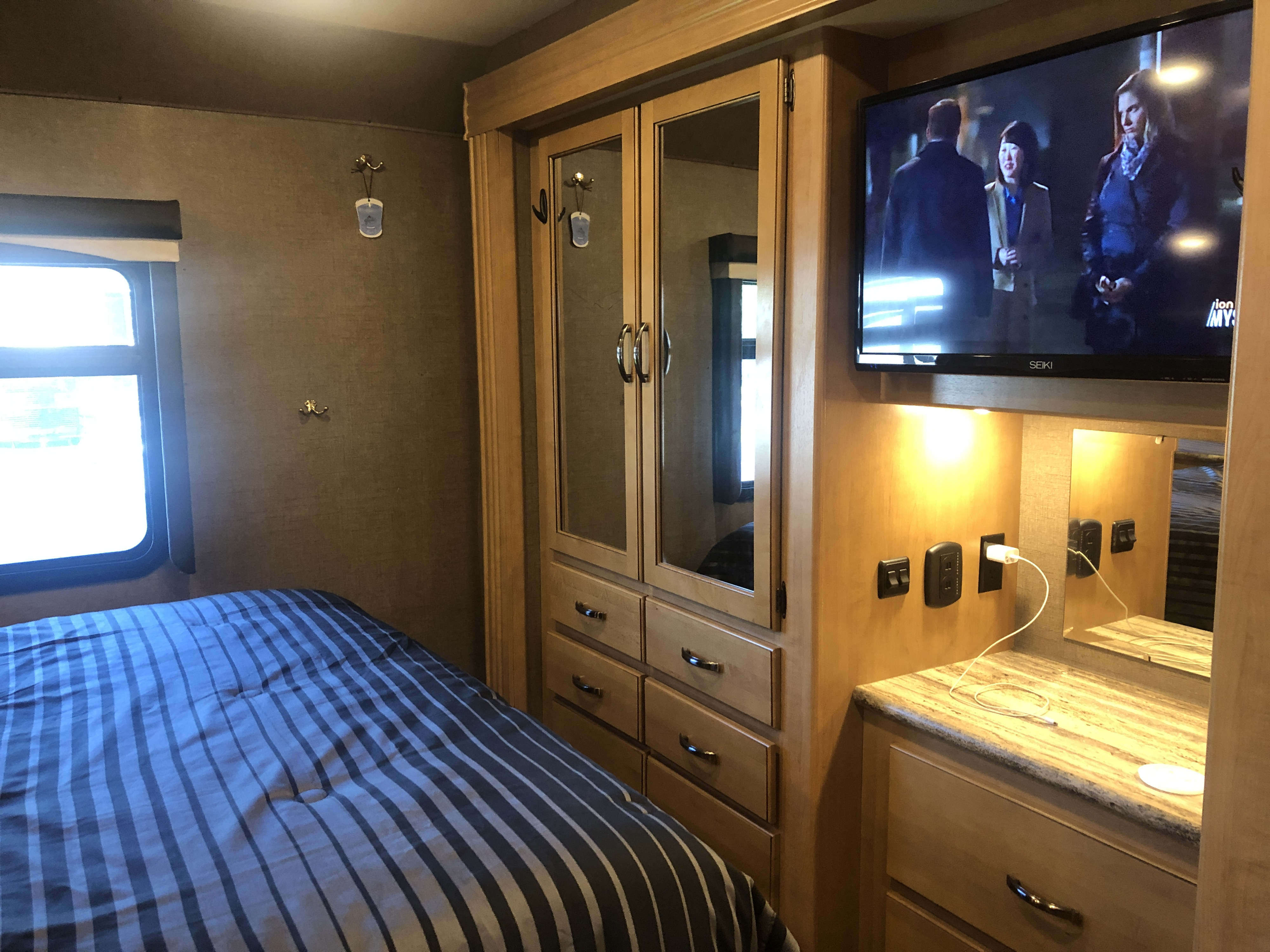 RV rental bedroom with striped bed, mirrored wardrobe, TV, window, and convenient outlets.. Thor A.C.E. 2017